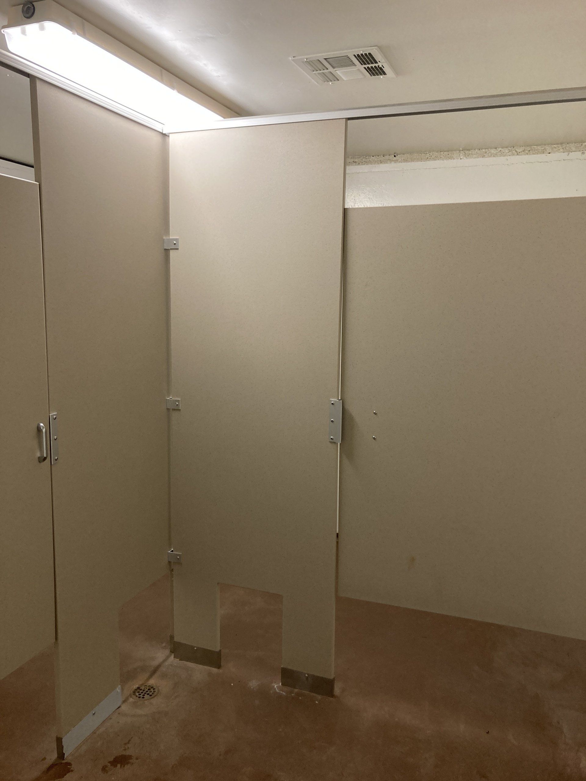 Empty public restroom with light-colored stalls. A single stall door is open.