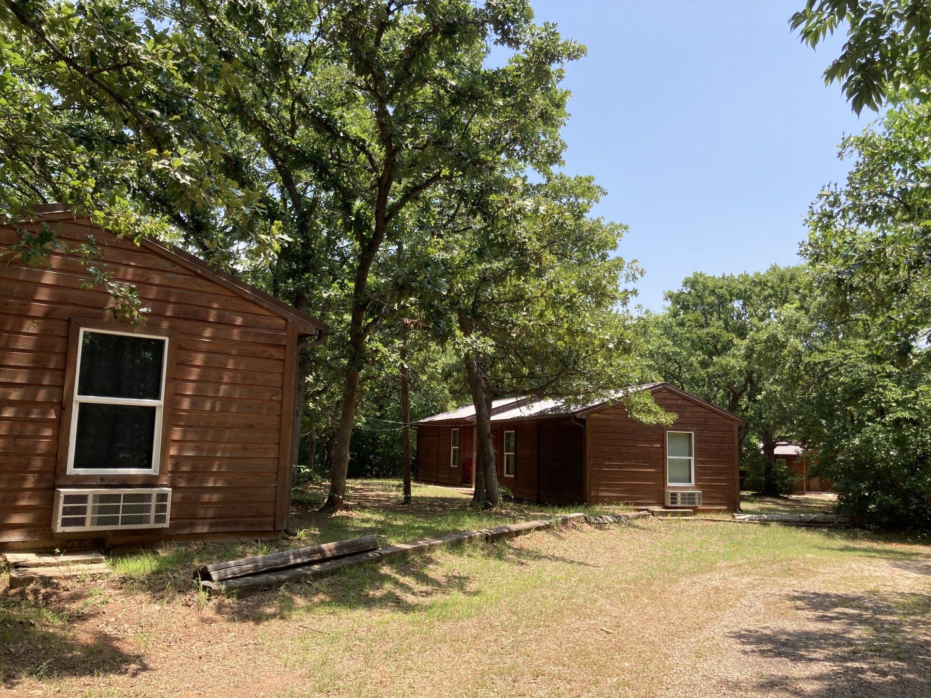 Brown cabins nestled among trees on a sunny day.