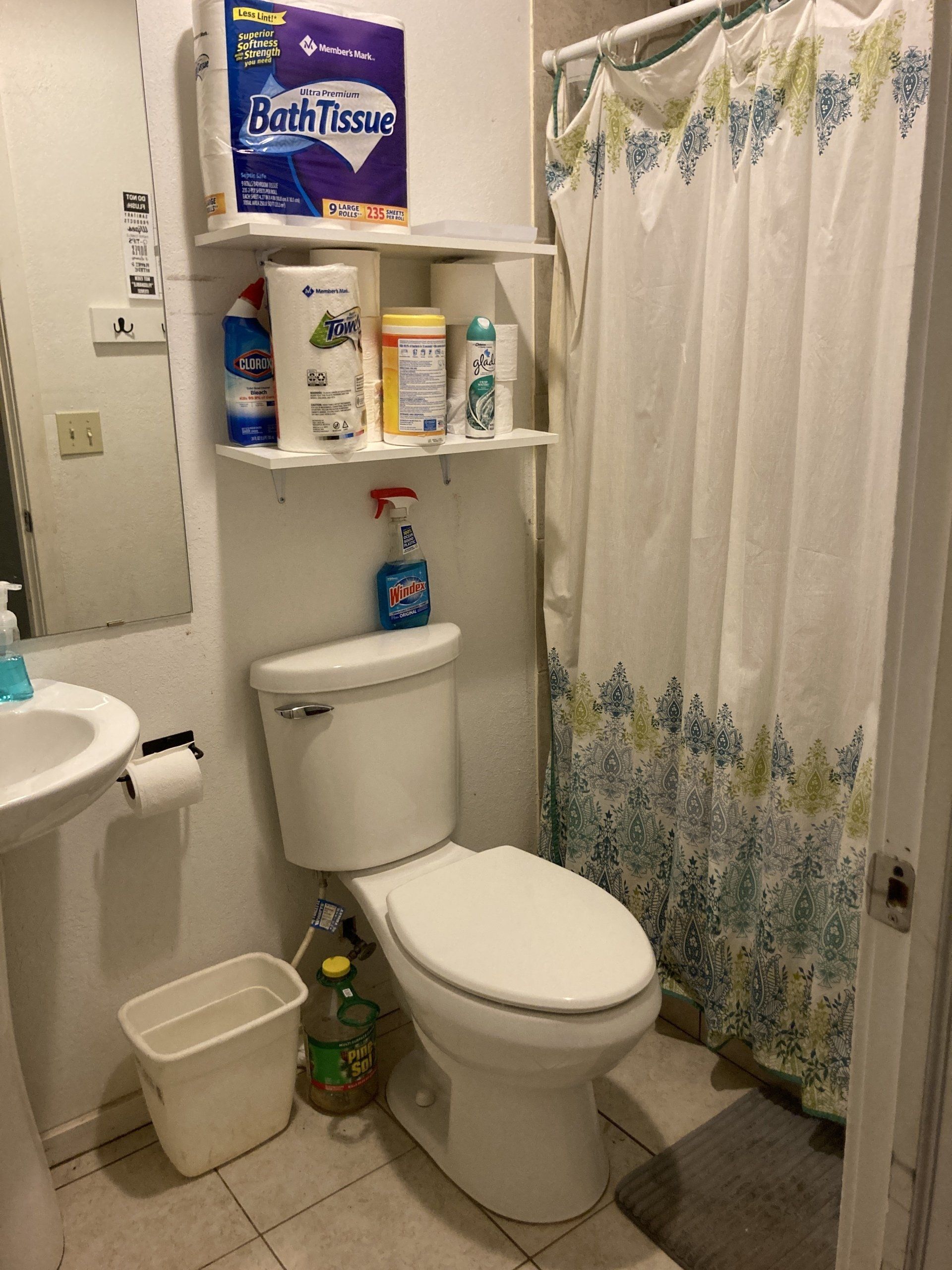 Small bathroom with toilet, shower, sink, and storage shelves.