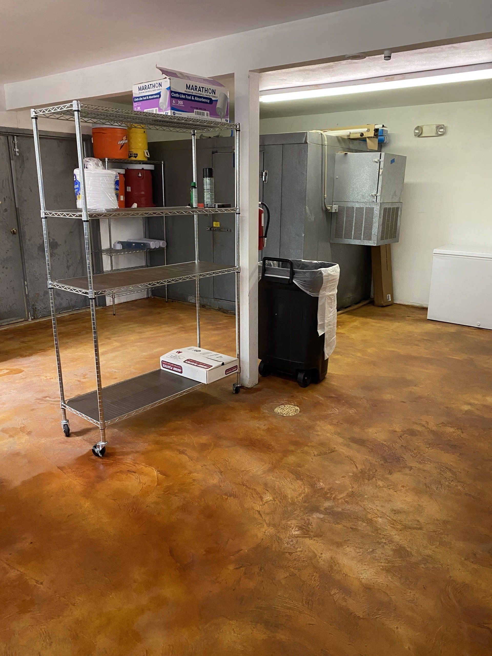 A storage area with metal shelving, paint cans, and a stained concrete floor.