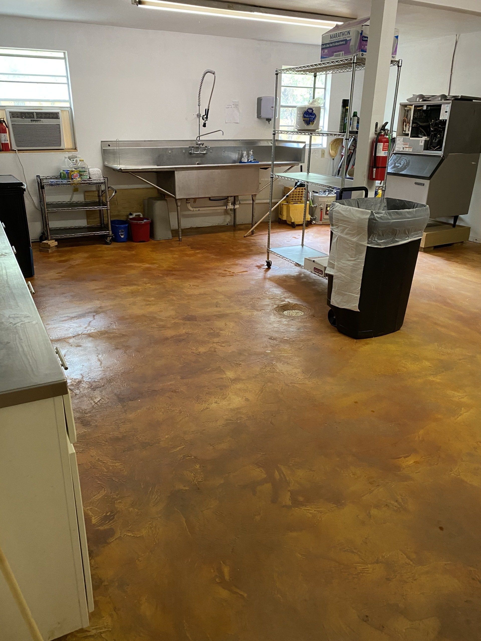 Commercial kitchen with stainless steel sinks and equipment, reddish-brown floor.