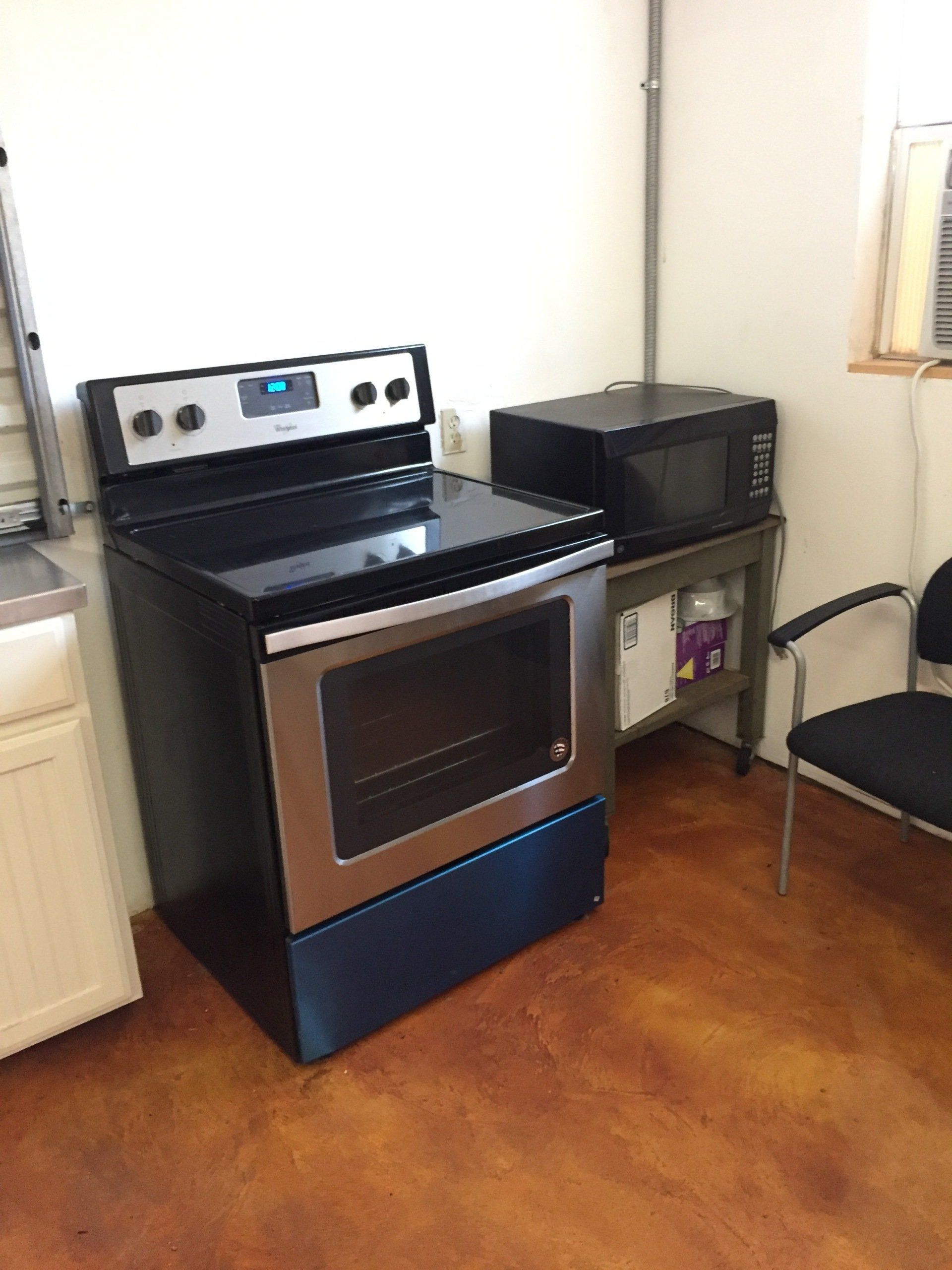 Stainless steel oven and microwave in a small kitchen. Brown floor, white walls.