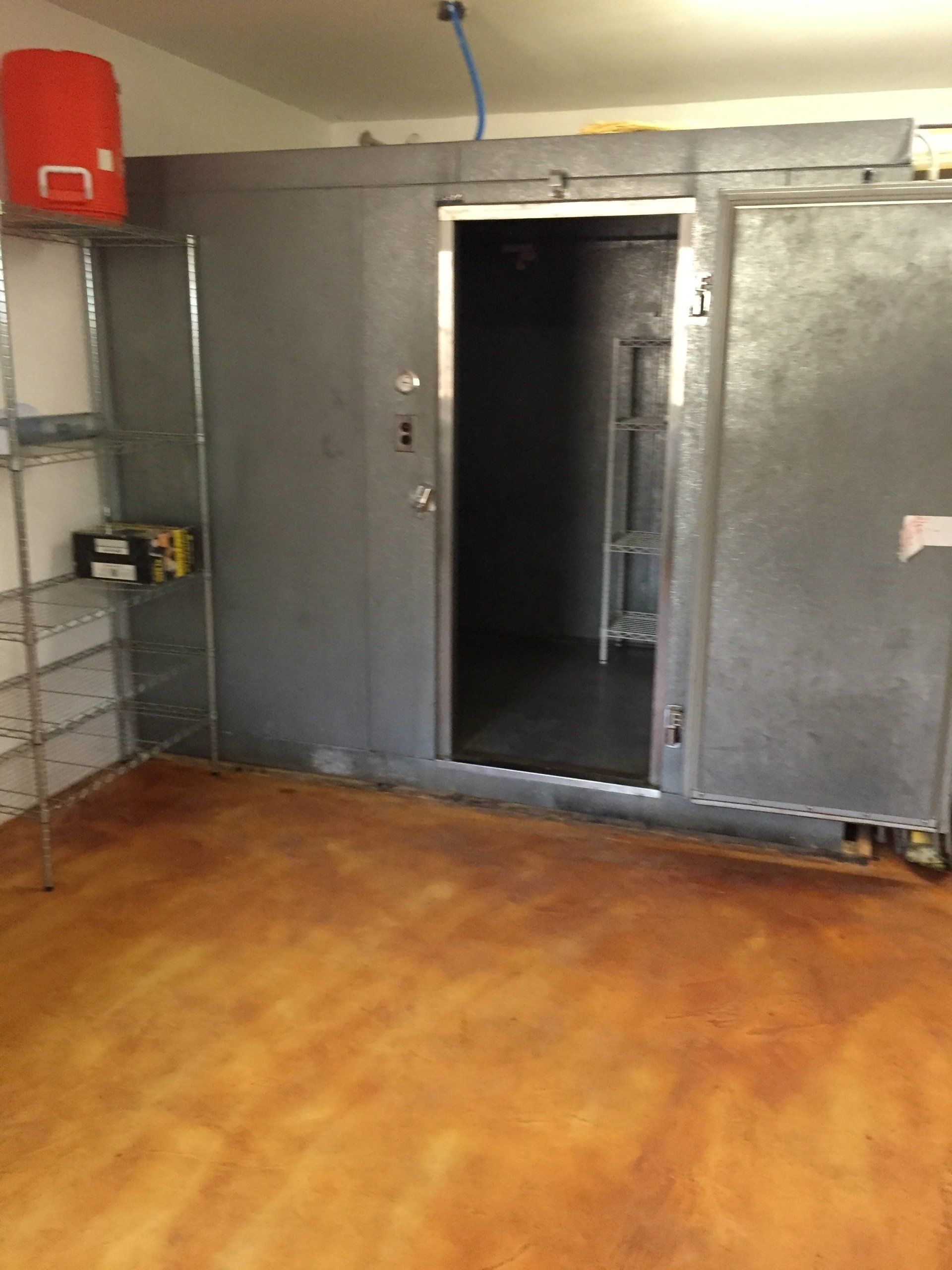A large, gray walk-in vault with an open door in a room with a stained, reddish-brown floor.