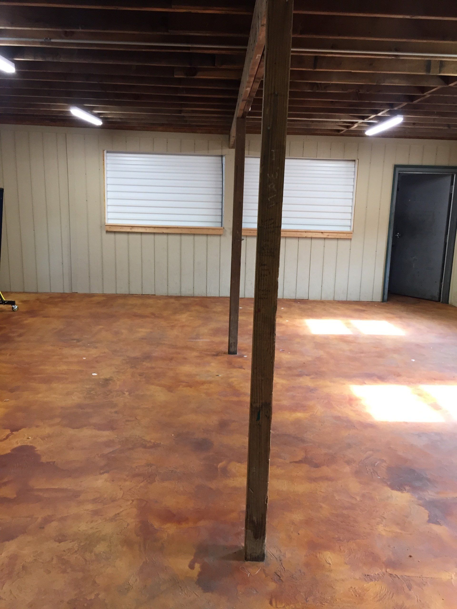 Interior of a room with stained concrete floor, wooden beams, windows, and a door.