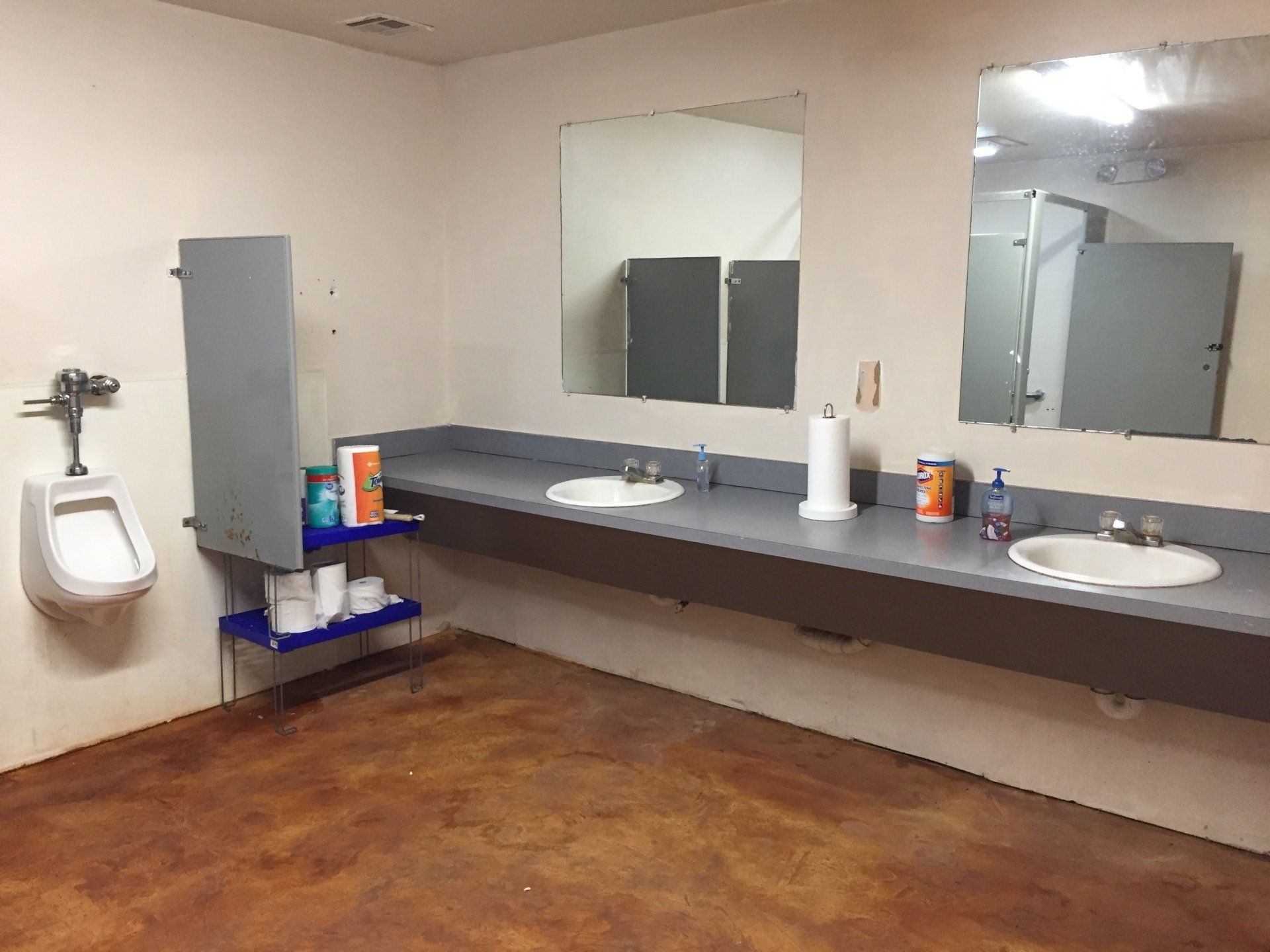 Public restroom with urinals, sinks, and stalls. Beige walls, brown floor, and gray countertops.