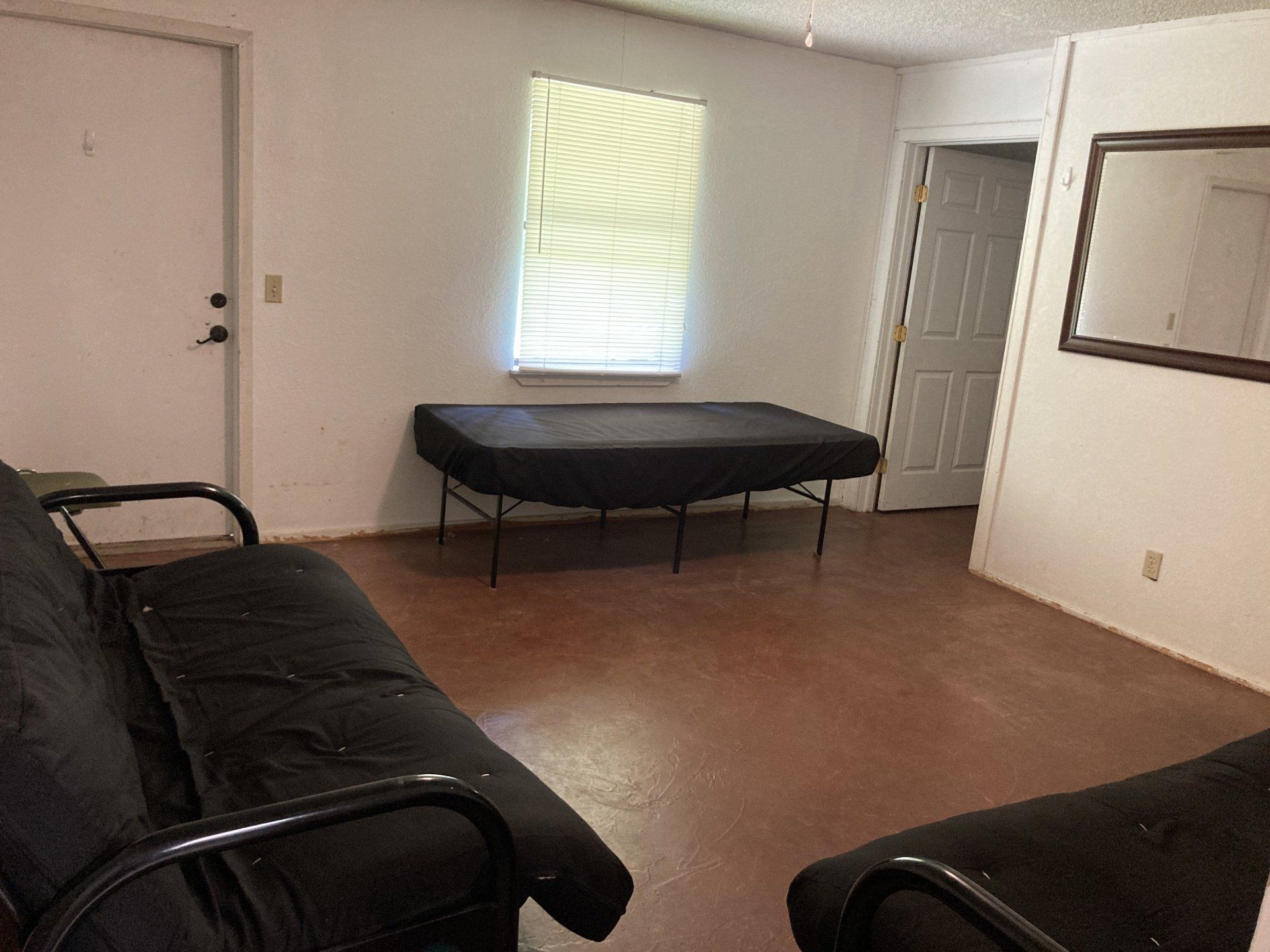 Room with dark furniture, bed, and door. Window with blinds, brown floor, white walls.