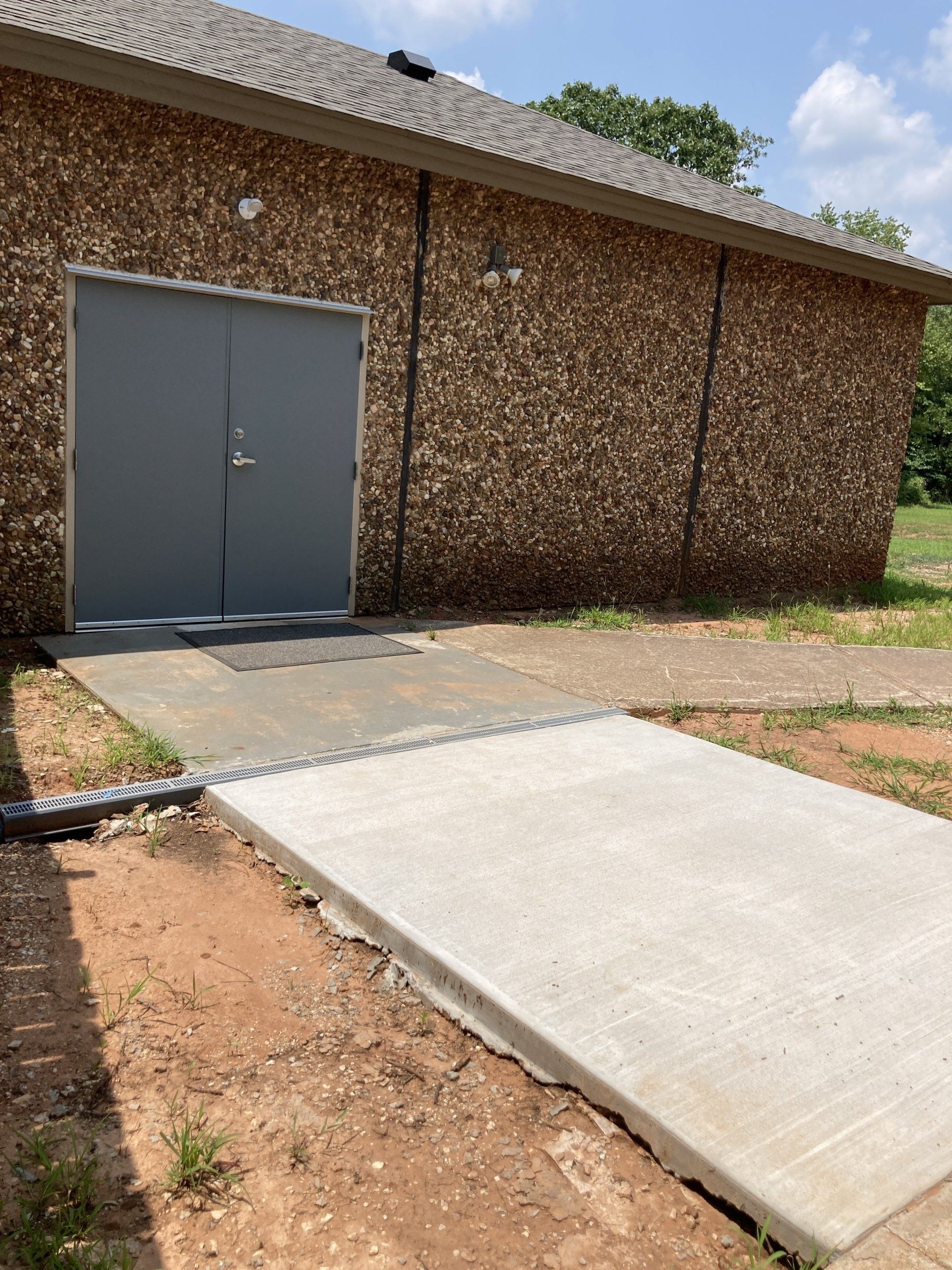 Gray double doors on a brown stone building with a concrete ramp and sidewalk.