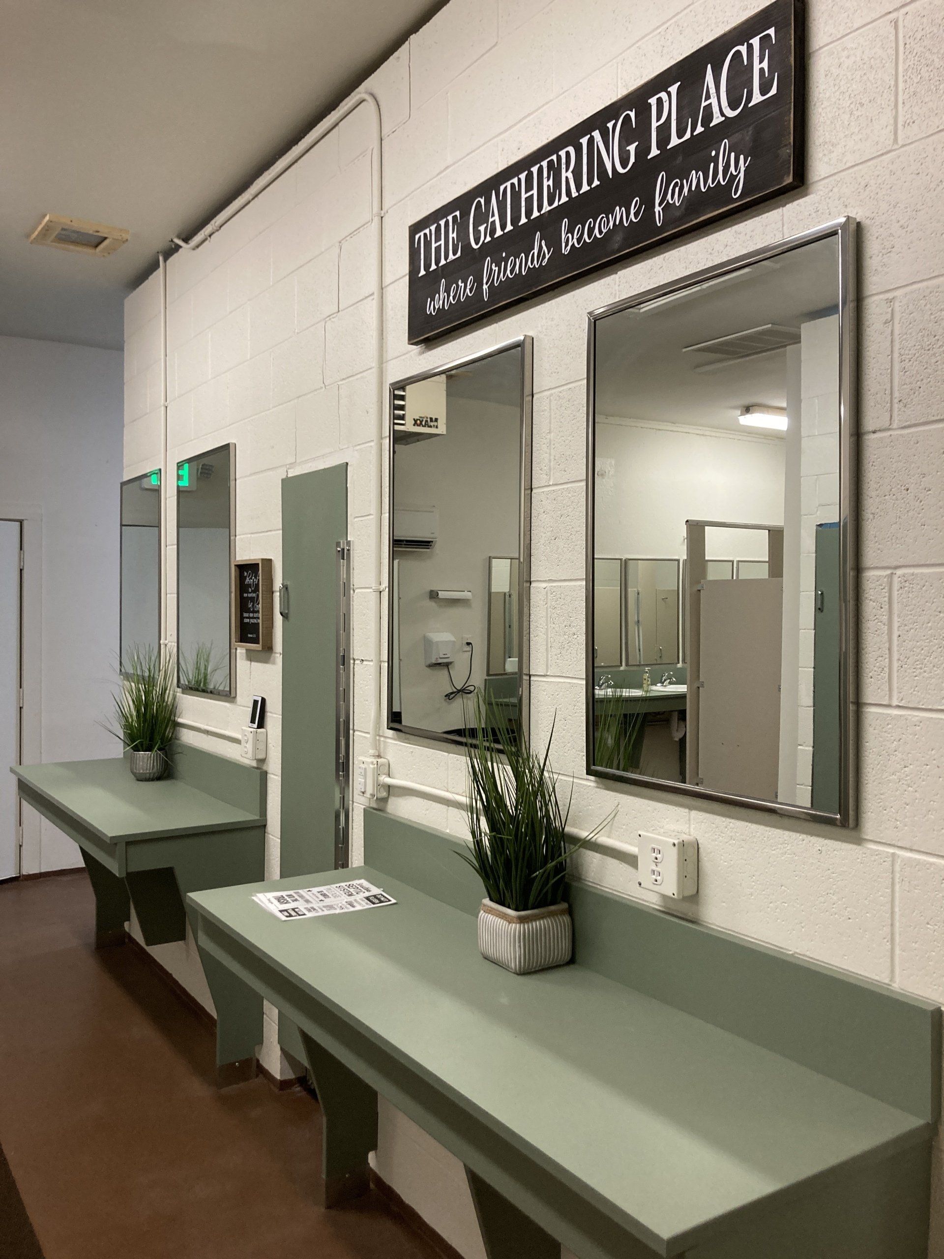 Public restroom with mirrors above sage green counters. Includes a sign that reads, 