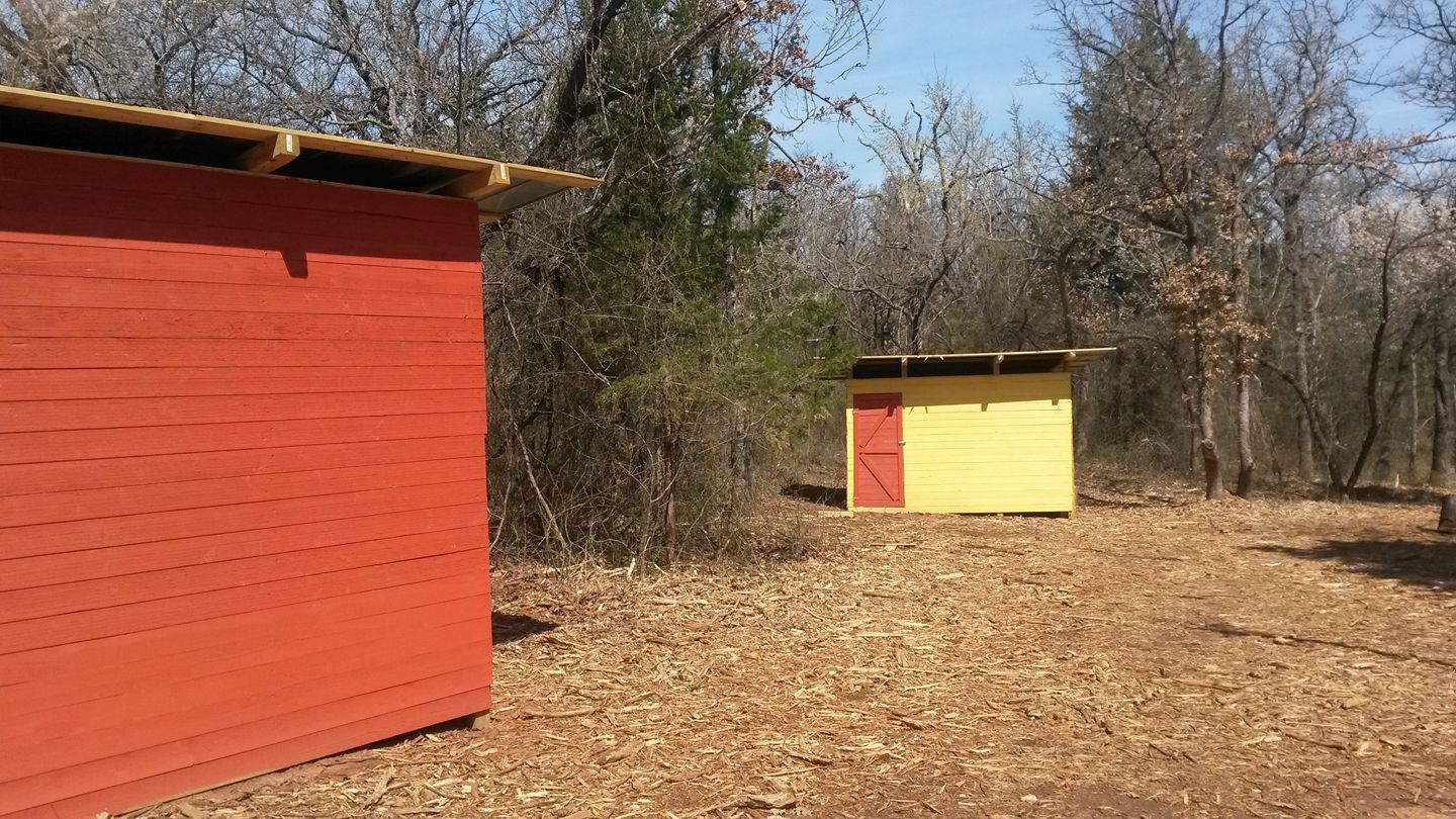 Two colorful wooden sheds in a wooded area; one red, one yellow.