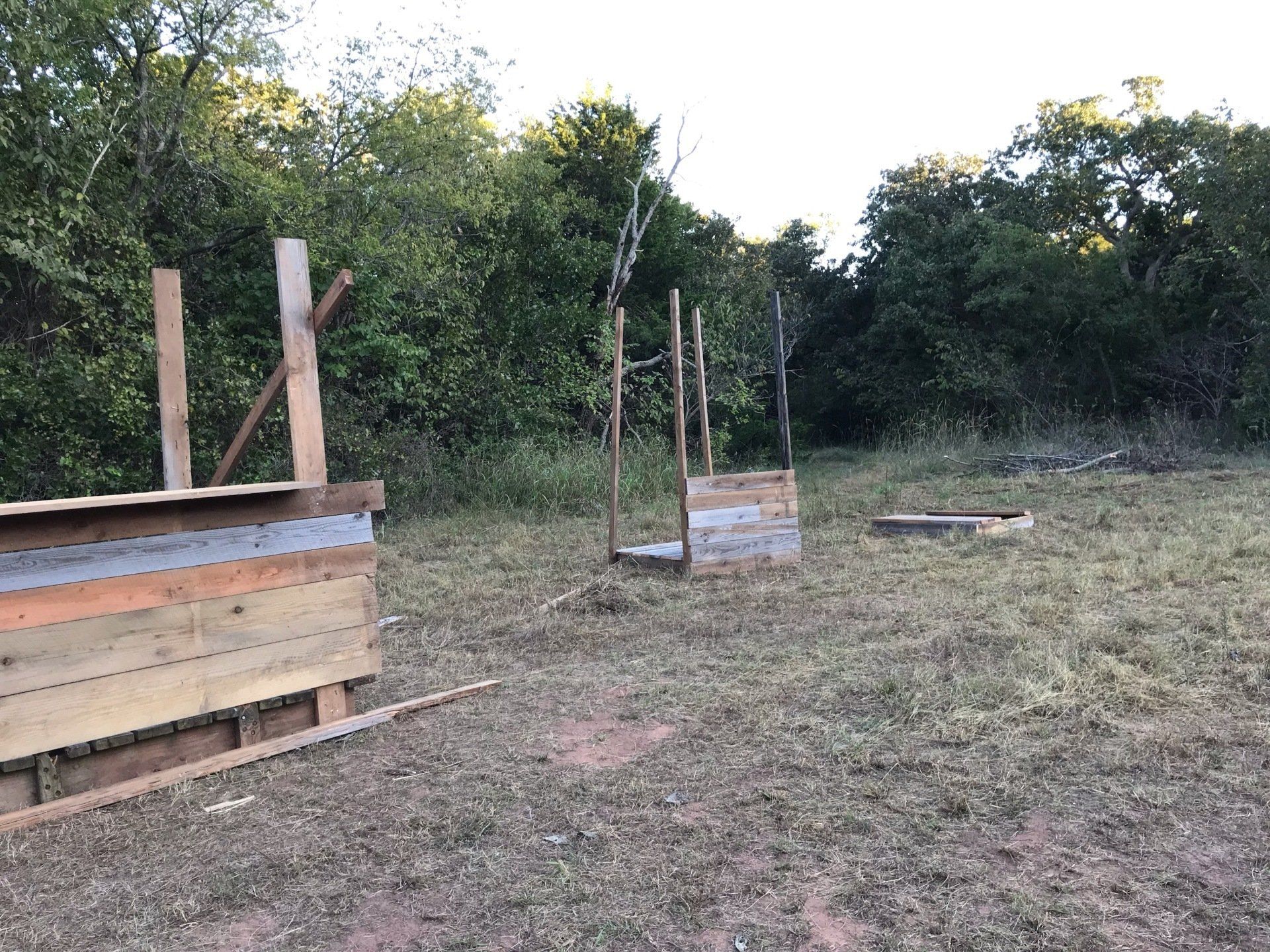 Wooden structures built outdoors in a grassy area, surrounded by trees.