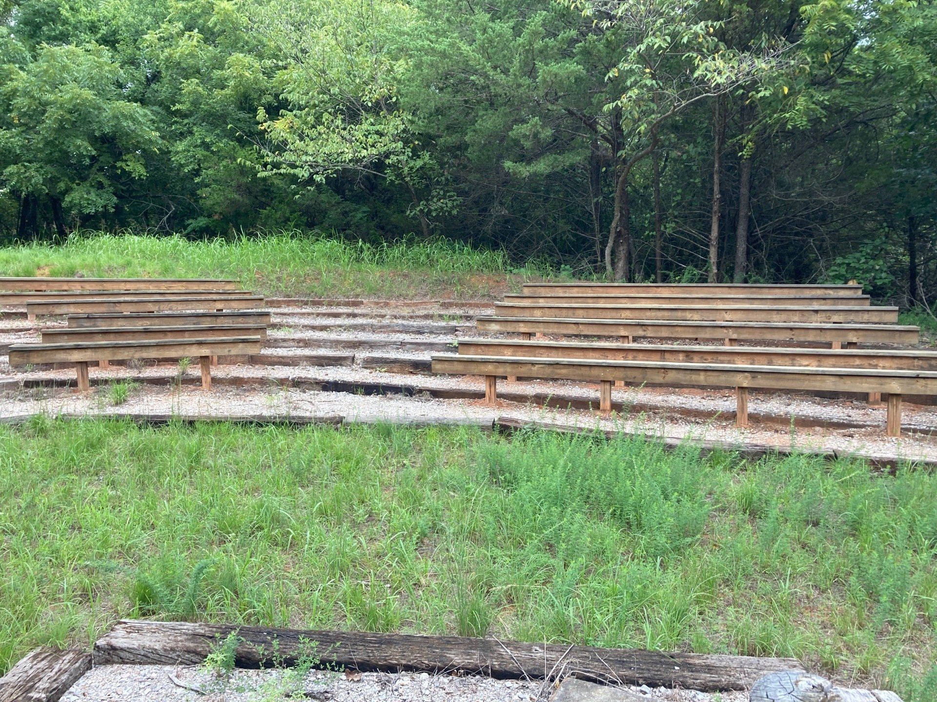 Outdoor amphitheater with wooden benches tiered on a grassy hillside, trees in the background.