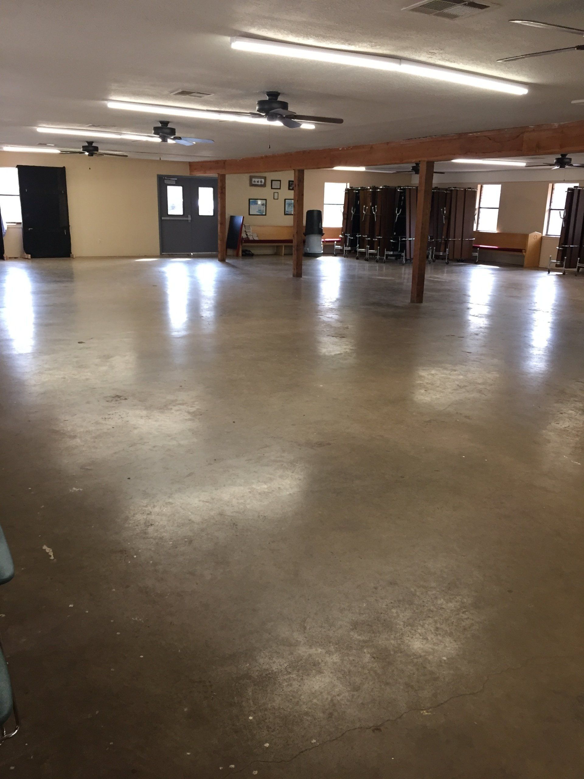 Large empty room with a polished concrete floor, support beams, and overhead lighting.