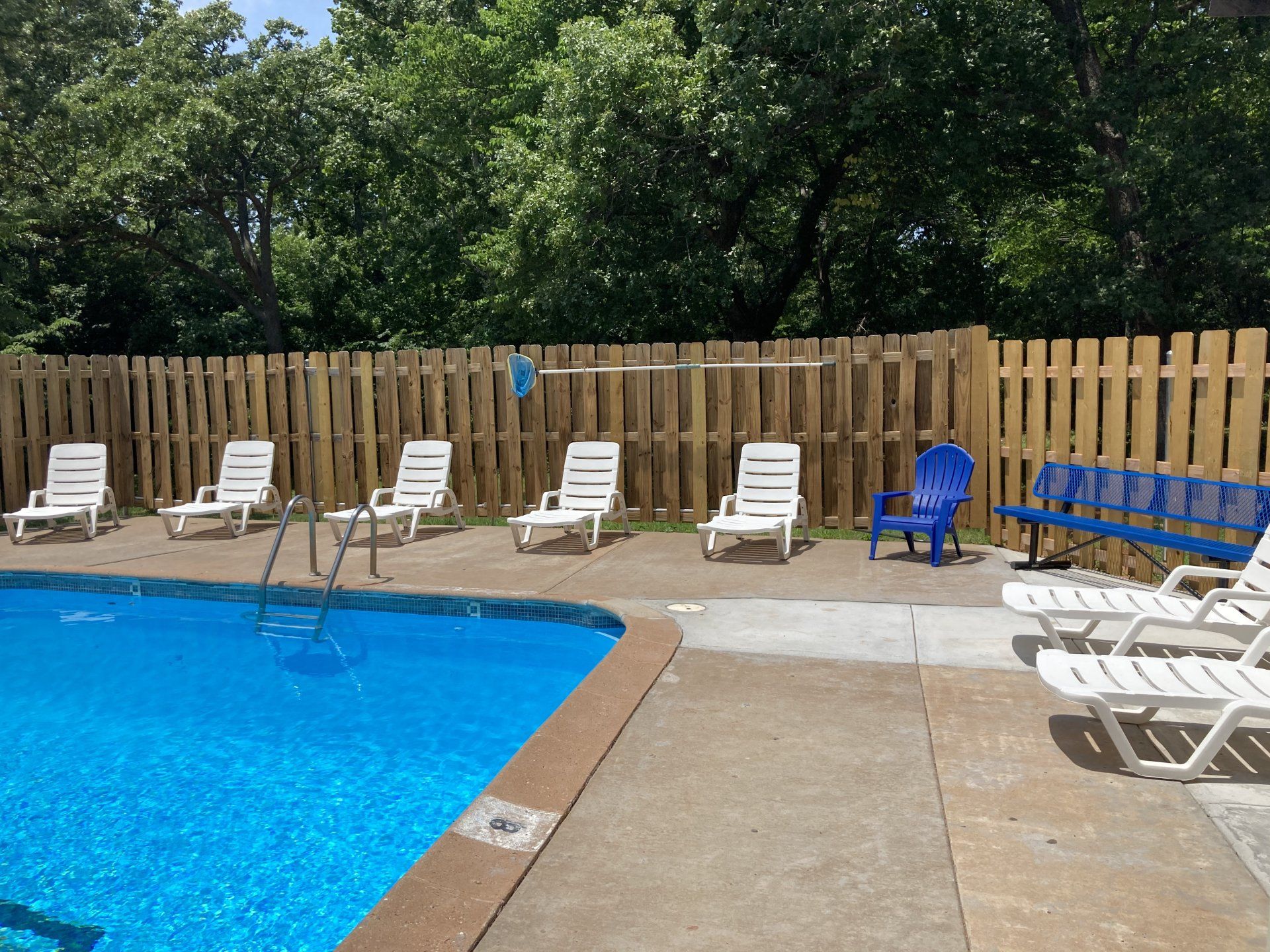 Poolside with white lounge chairs, blue benches, and a wooden fence.