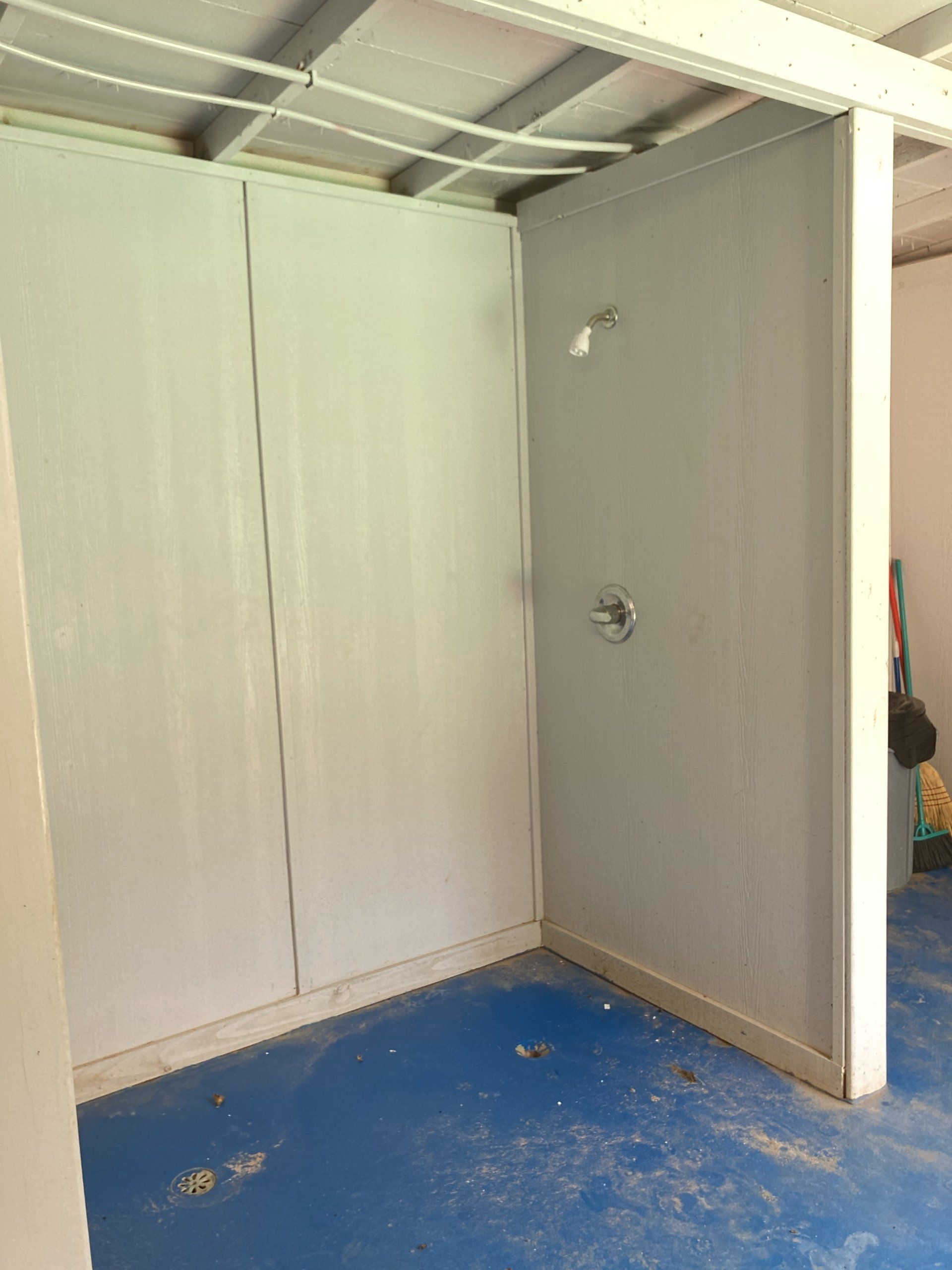 Gray-walled shower stall under construction with blue floor, plumbing fixtures installed.