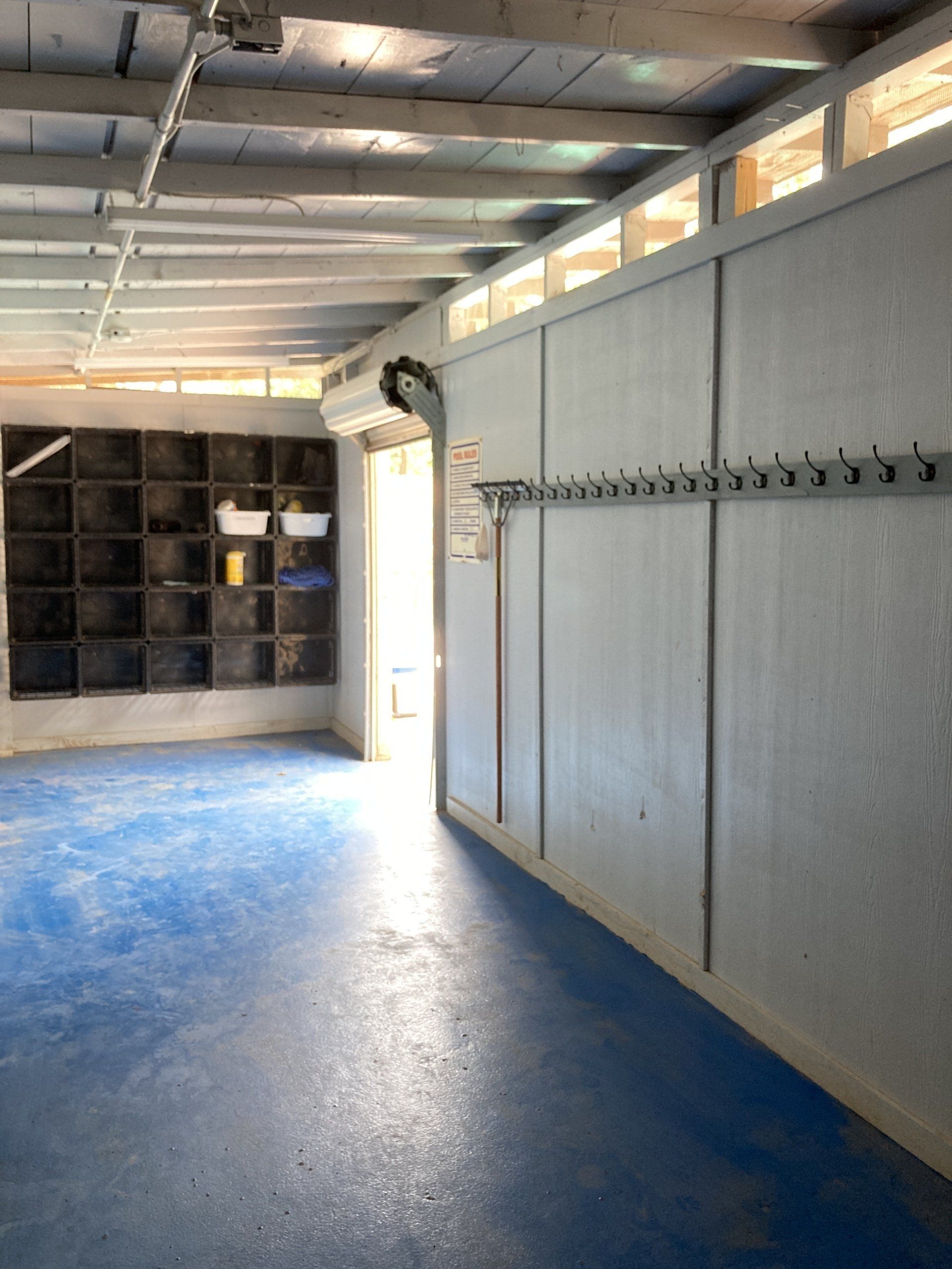 A garage with a blue floor, gray walls, and a roller door. There's a storage unit on the left.