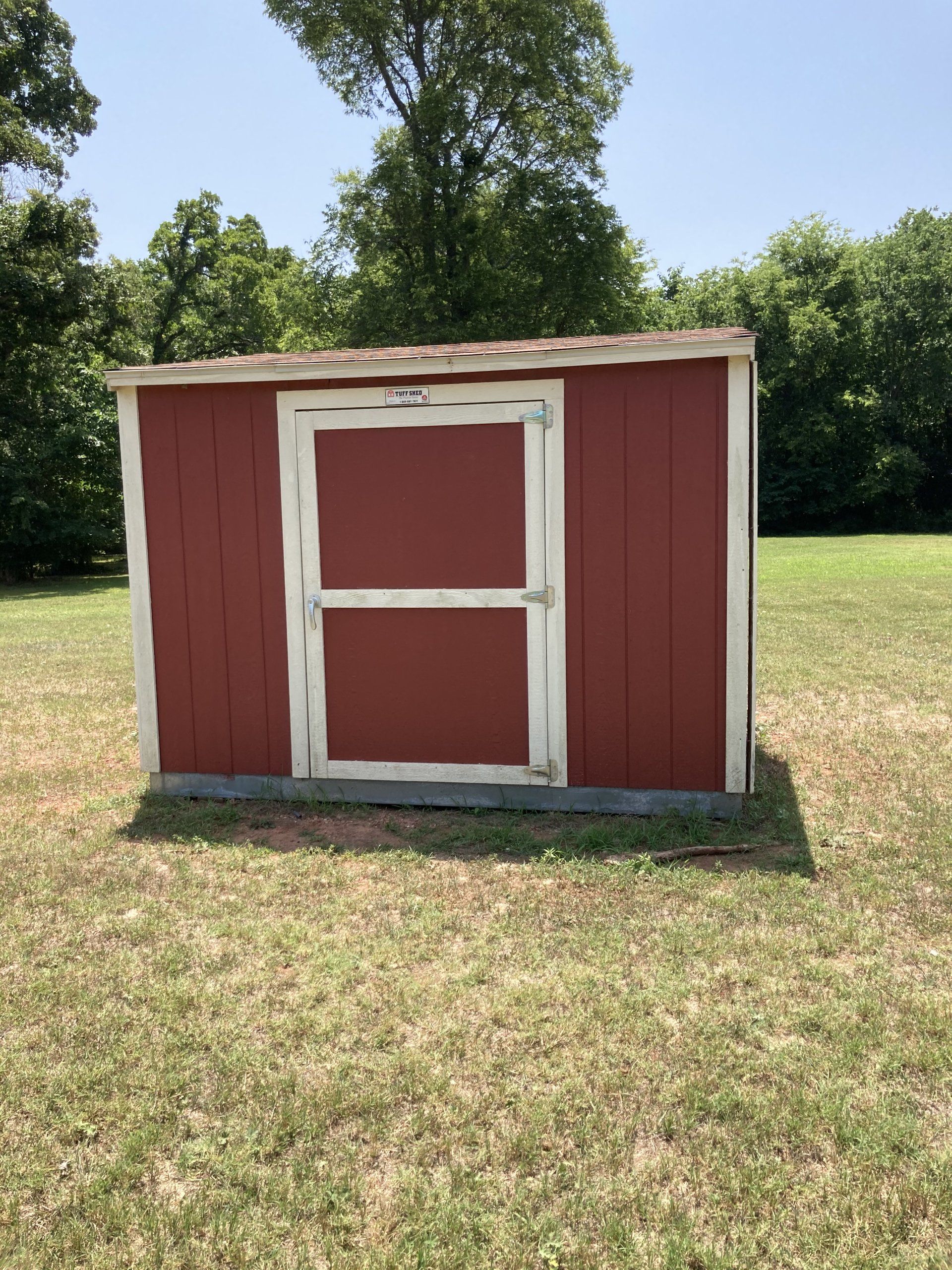 Red shed with white trim, standing on grass, with trees in the background.