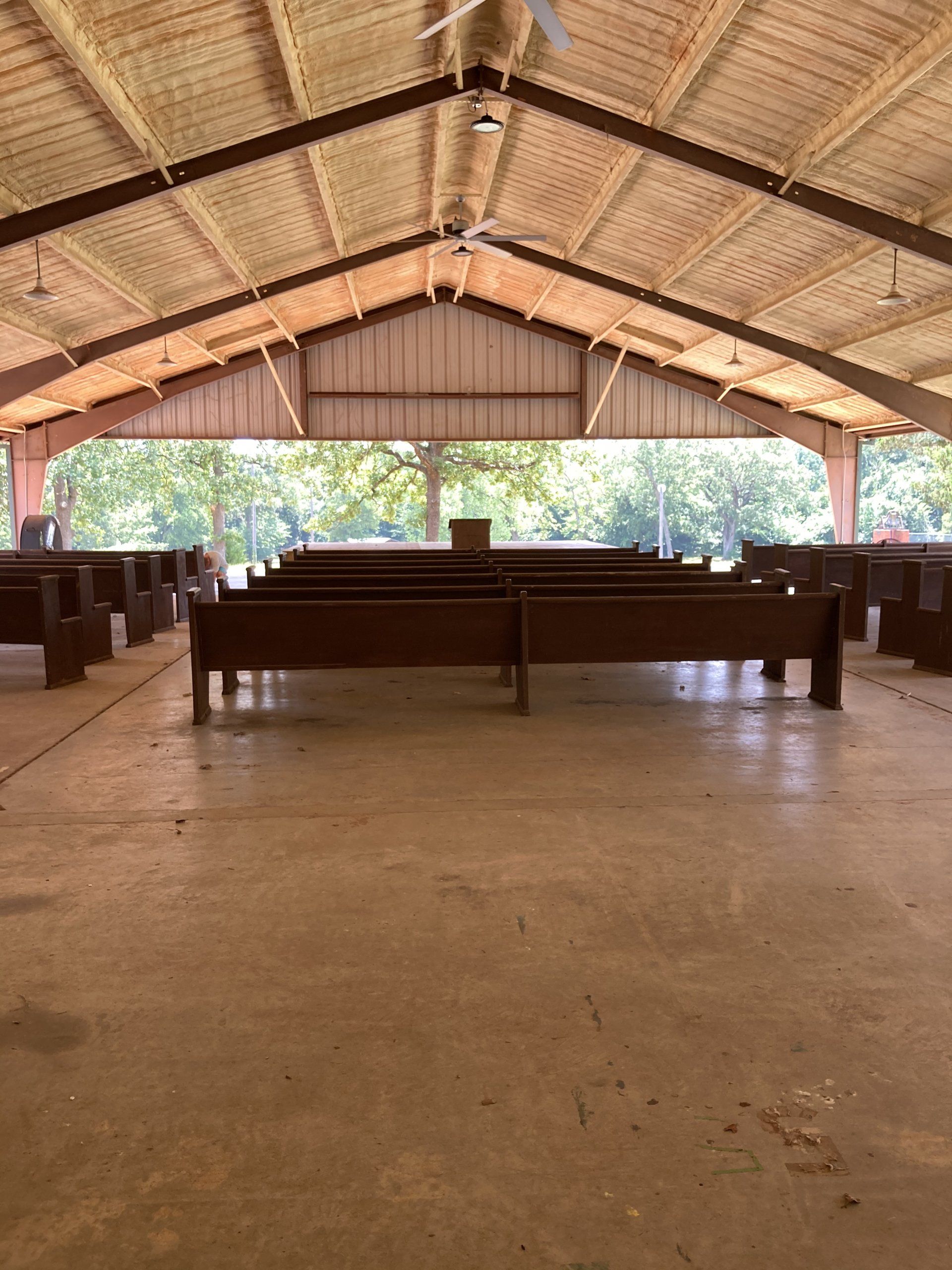 Open-air chapel with rows of wooden pews, high ceiling, and a simple pulpit.