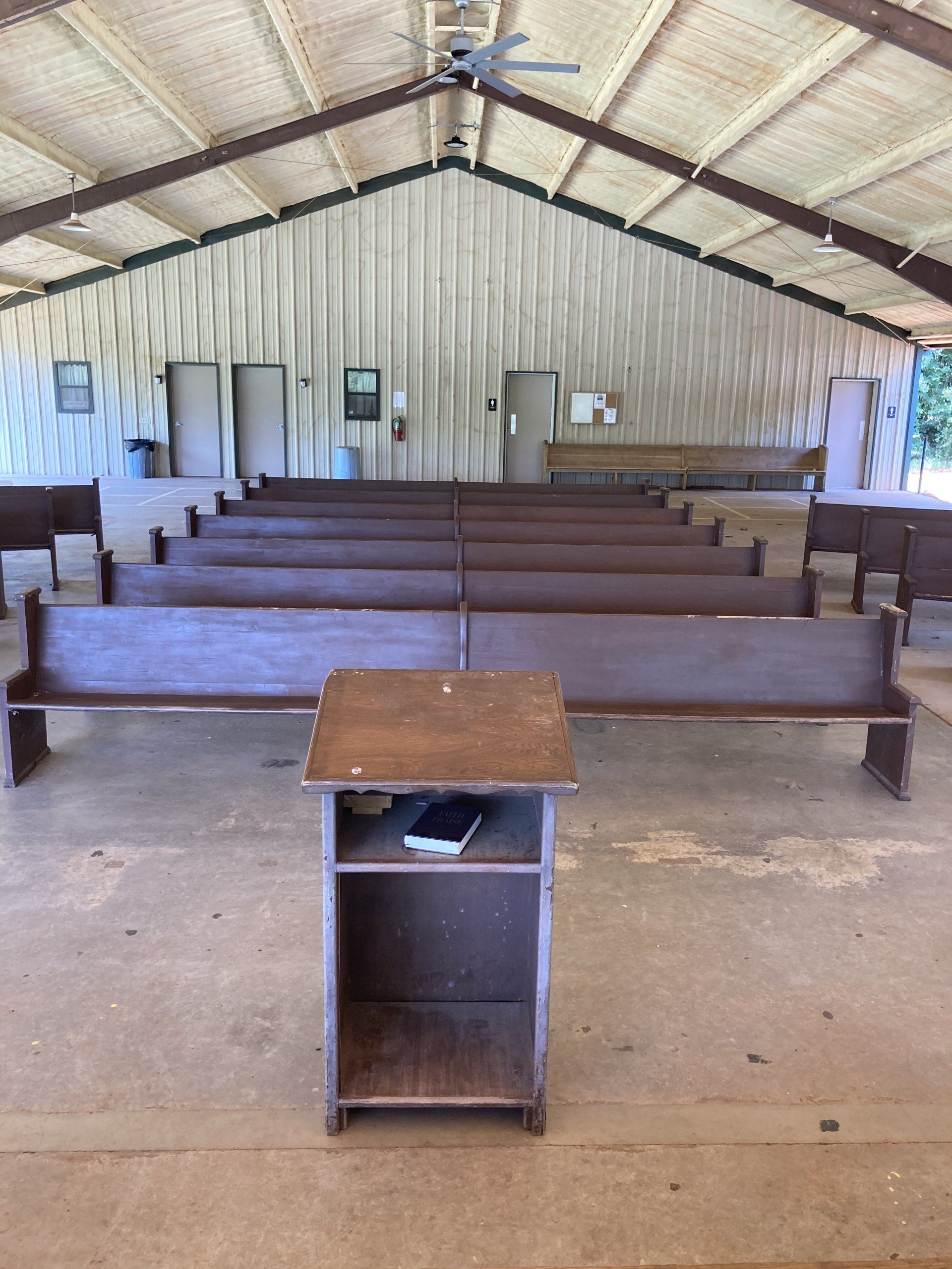 Wooden podium in front of rows of wooden benches in a covered, open-air structure.