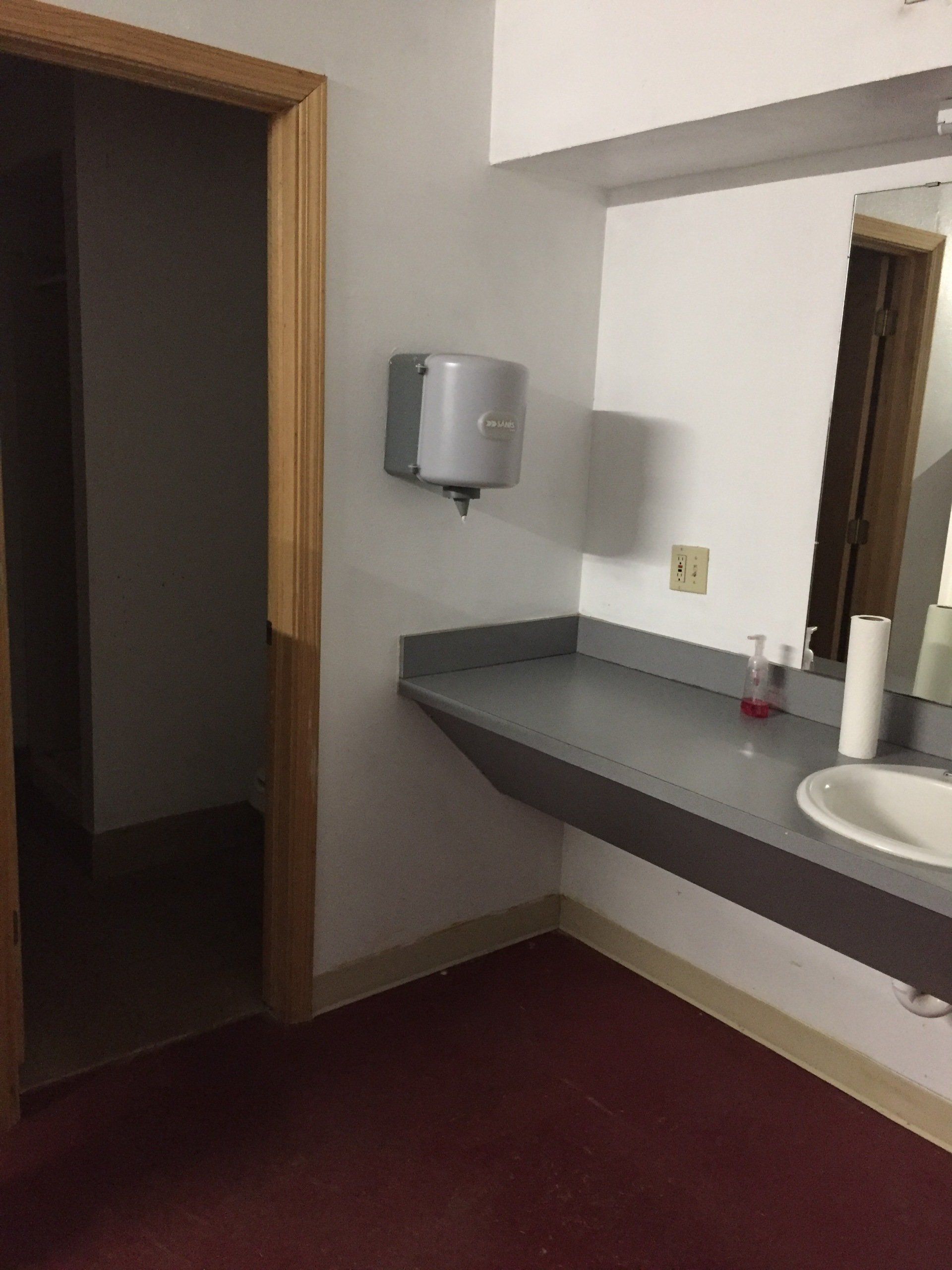 Bathroom with sink, paper towel dispenser, and open doorway on red carpet.