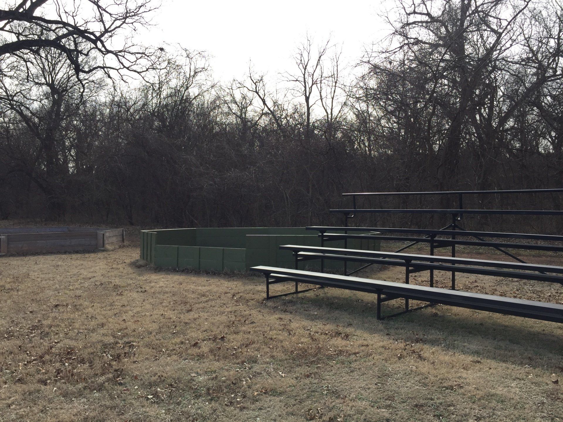 Outdoor amphitheater with rows of bench seating and a central stage area, surrounded by trees.
