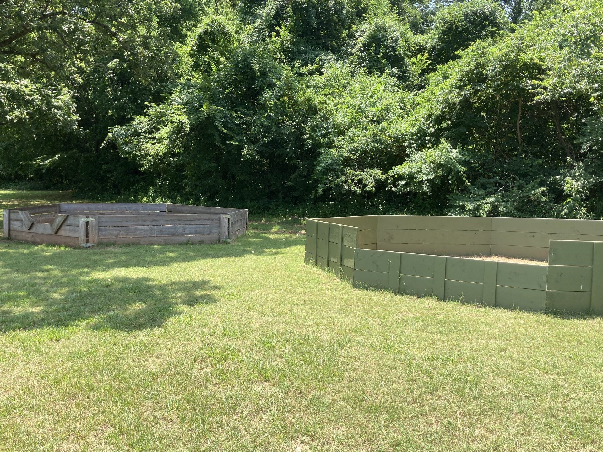 Two garden beds on a grassy lawn with a treeline backdrop. One is weathered wood; the other is green.
