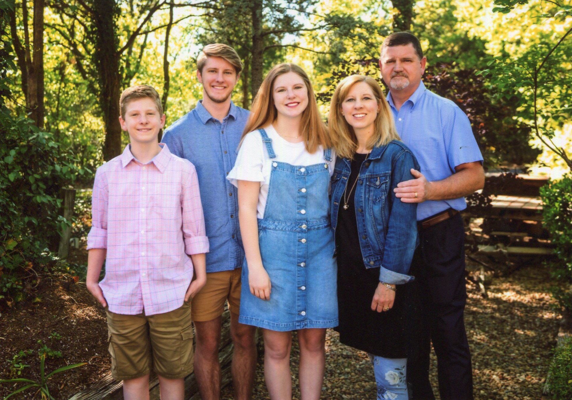 Family of five posing outdoors in front of greenery.