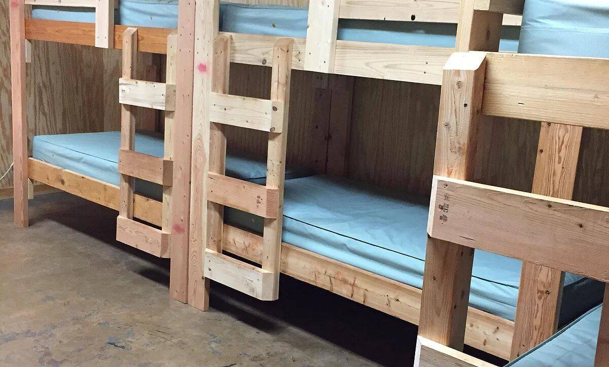Wooden bunk beds with light blue mattresses in a room with light-colored walls.