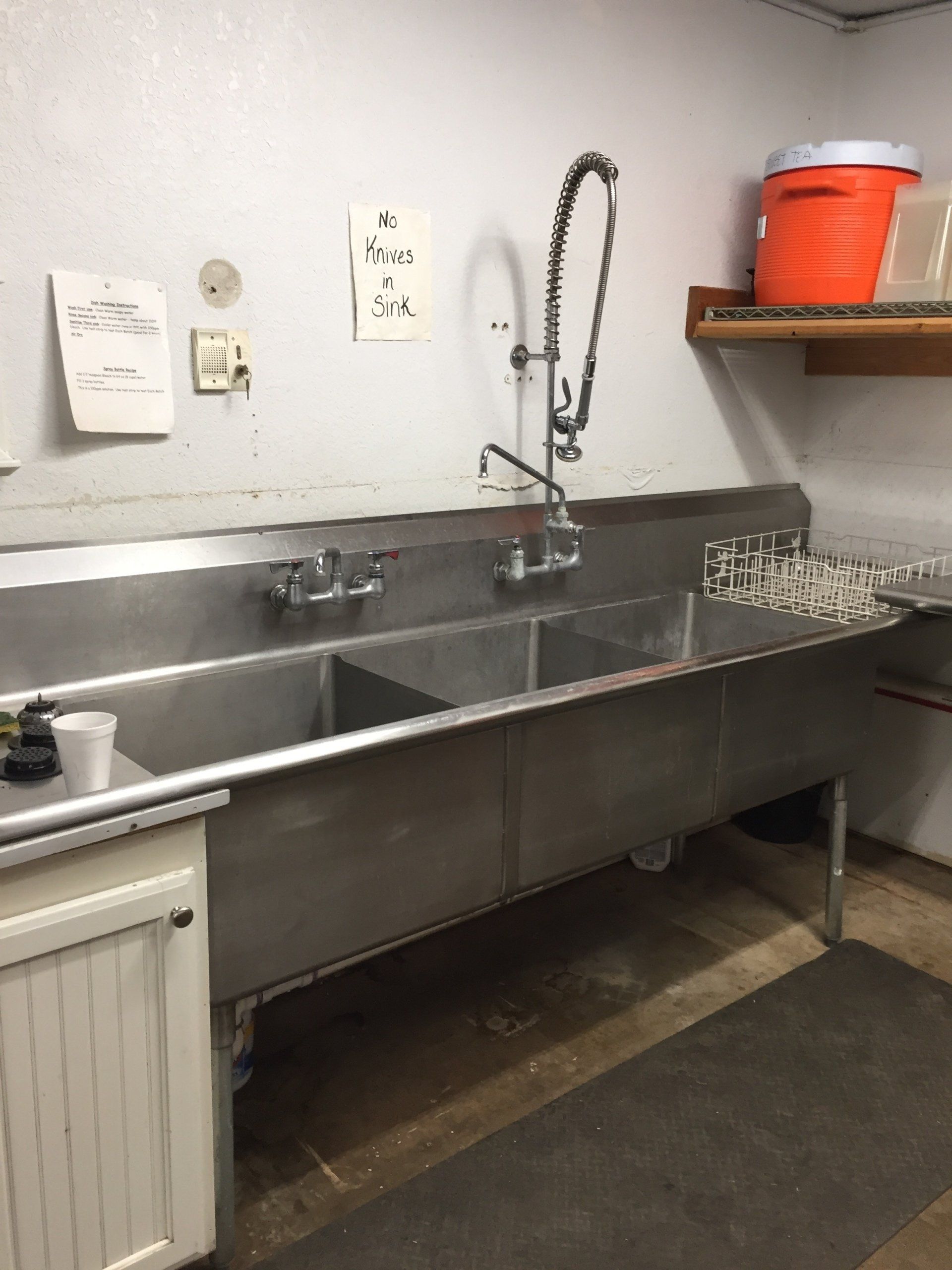 Stainless steel three-basin sink in a commercial kitchen with a high-arch faucet and spray nozzle.