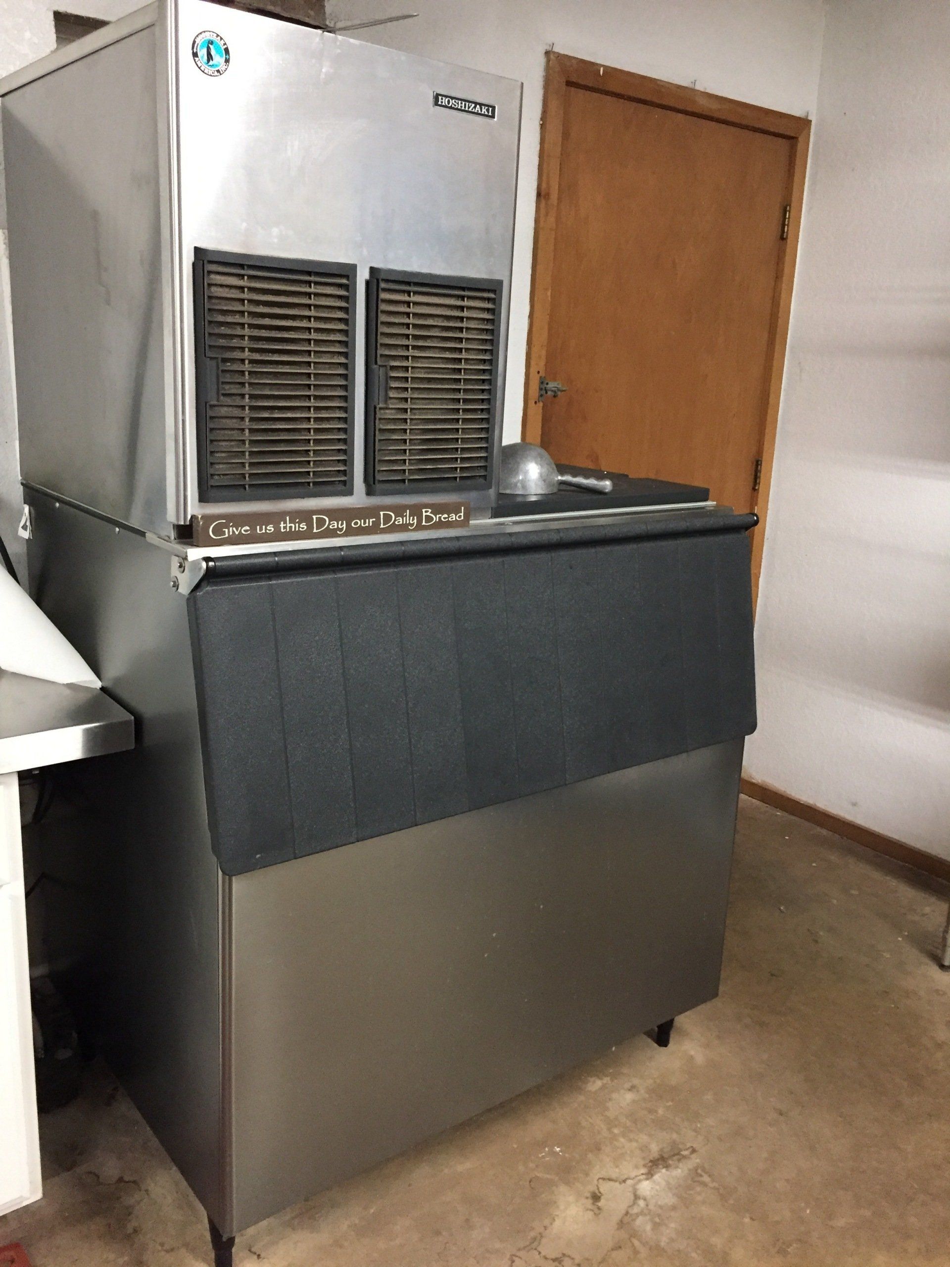 Stainless steel ice machine in a room with a closed wooden door.