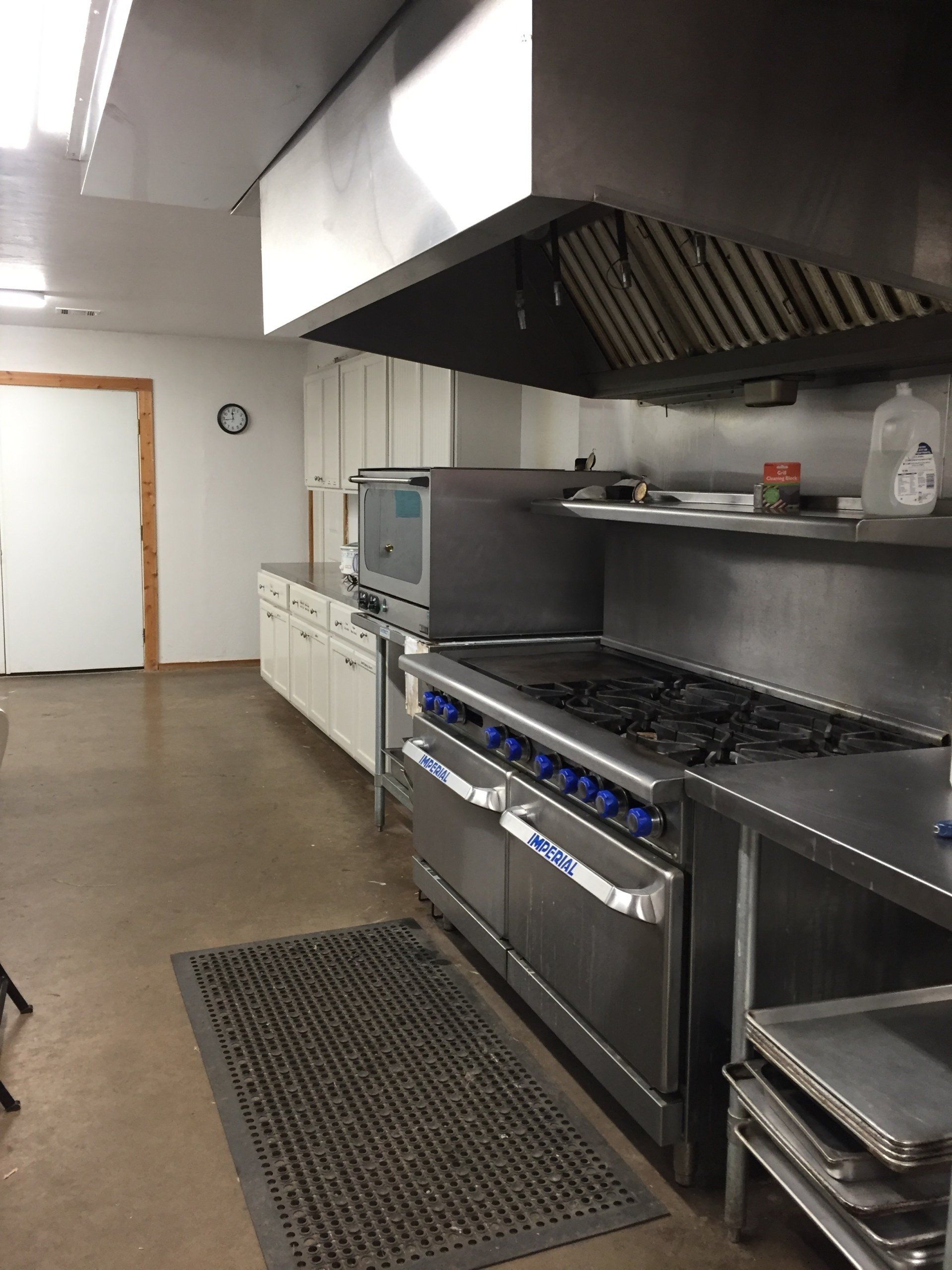 Commercial kitchen with stainless steel appliances, stove, vent hood, and cabinets.