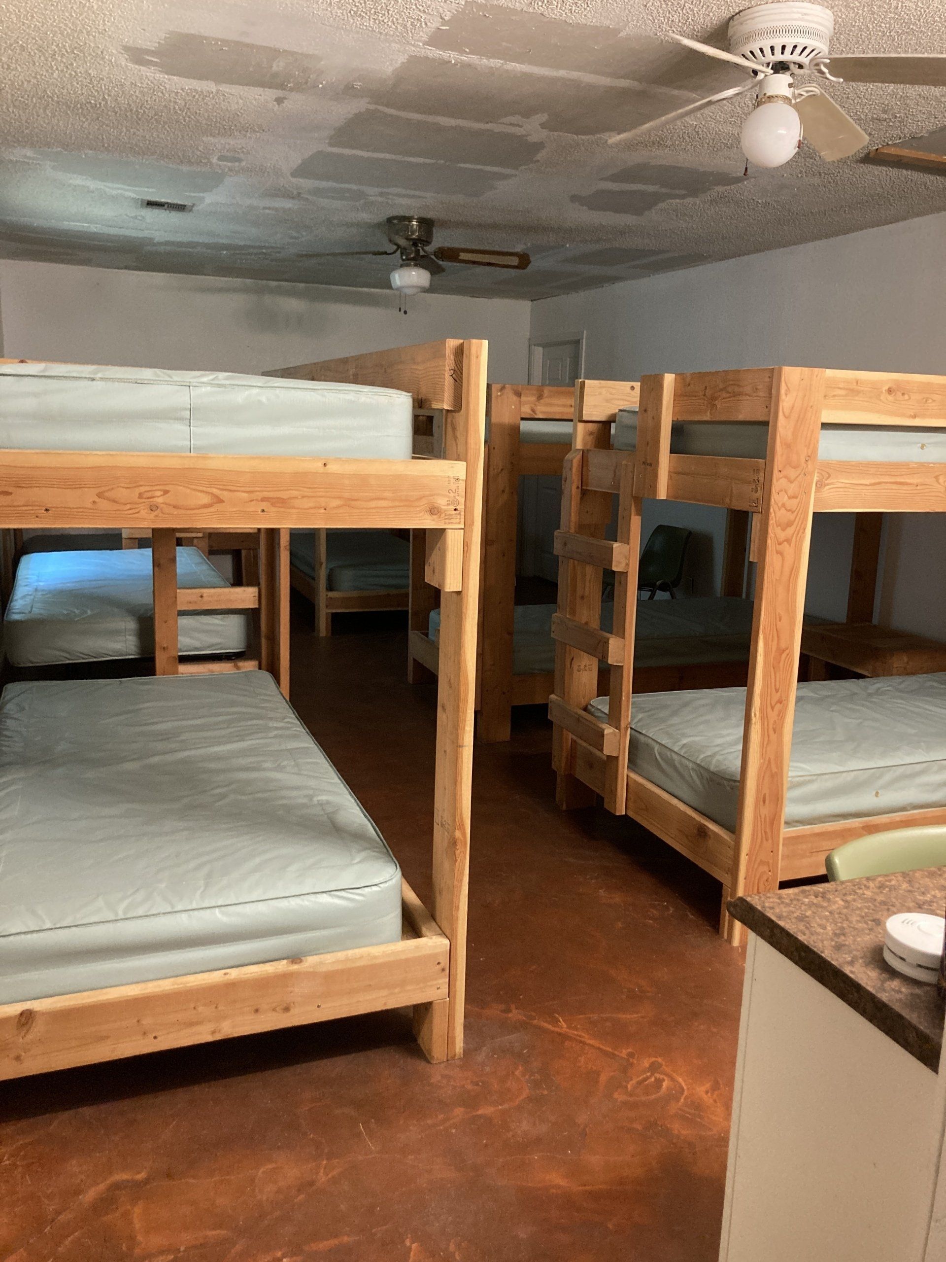Several wooden bunk beds in a room with a stained concrete floor and a ceiling fan.