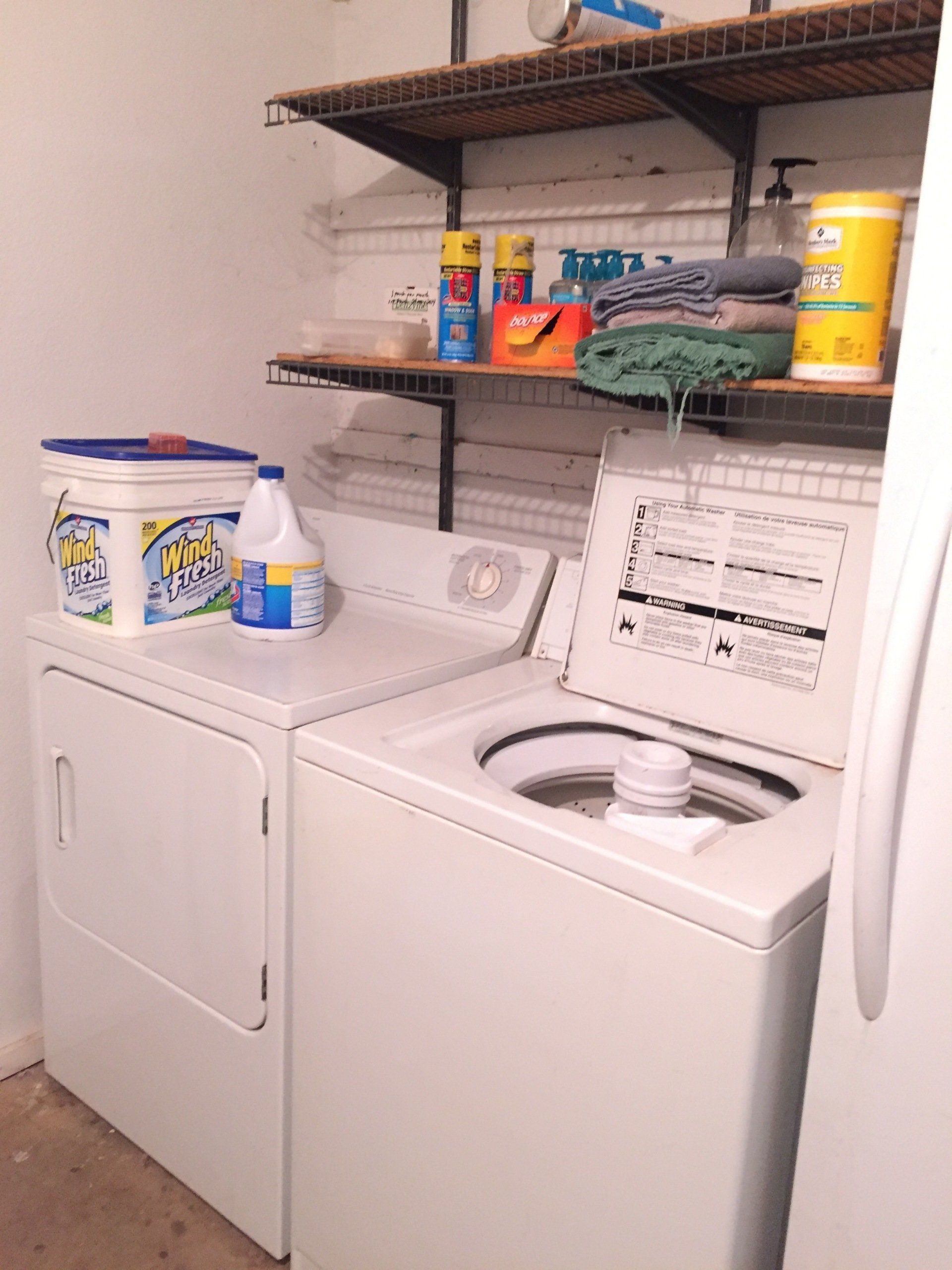 Laundry room with a dryer, washing machine, and shelves holding cleaning supplies and towels.
