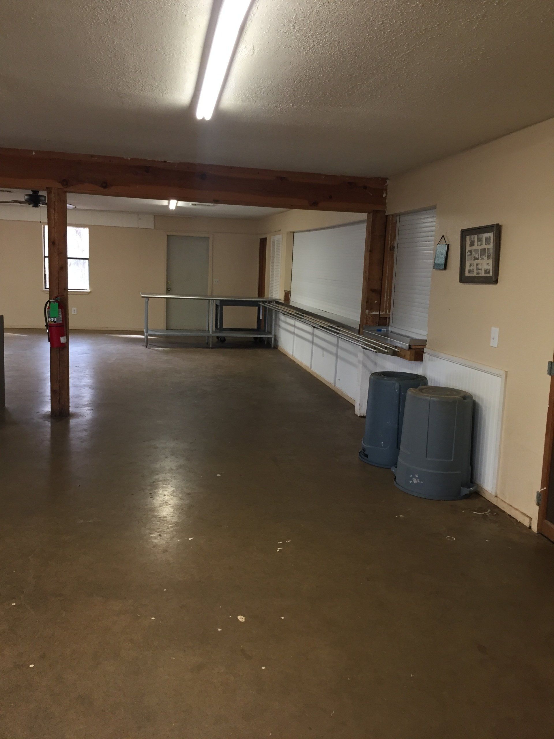 Empty room with brown flooring and tan walls, a light fixture, and wooden support beams.