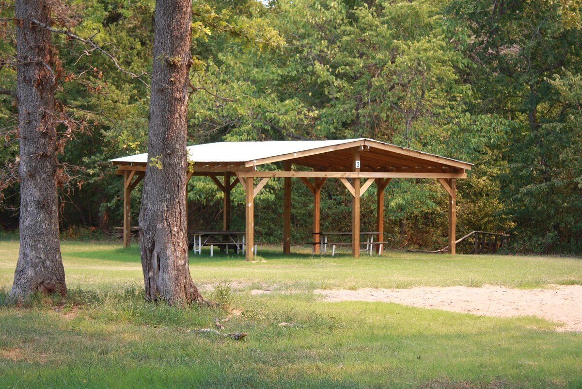 Picnic shelter in a grassy park, with trees in the background, a gravel path.