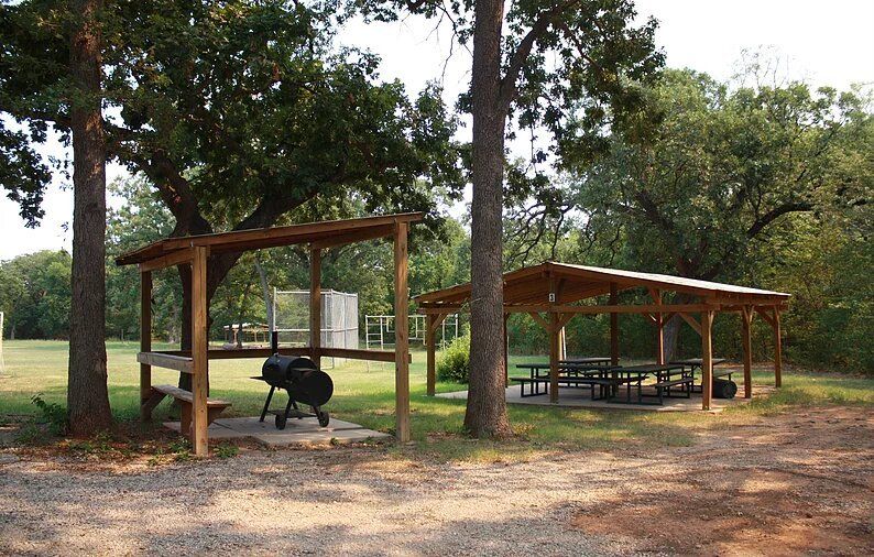 Picnic area with two covered shelters, grill, tables, and trees.