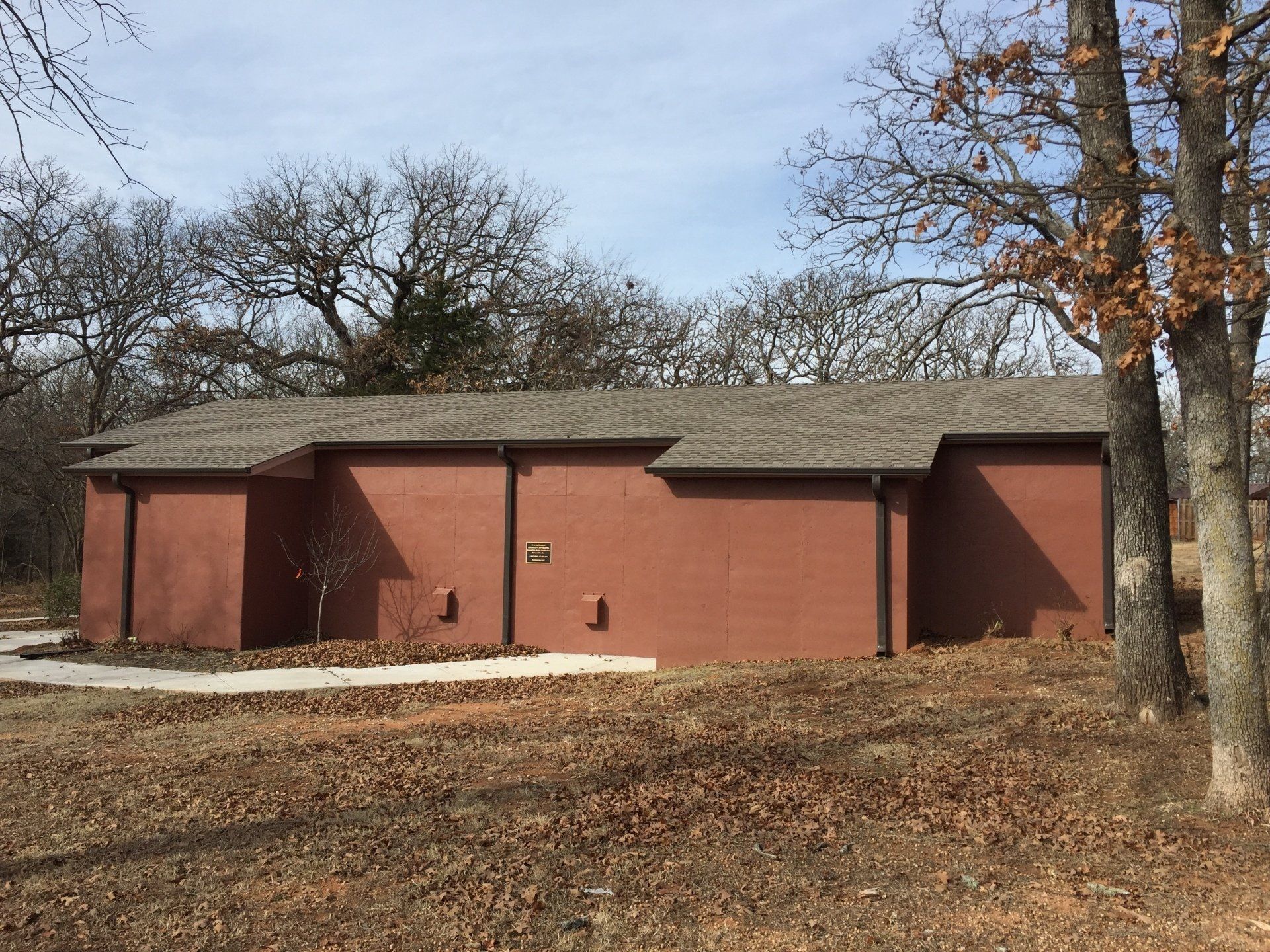 Red brick building with a flat roof, surrounded by trees and dry grass.