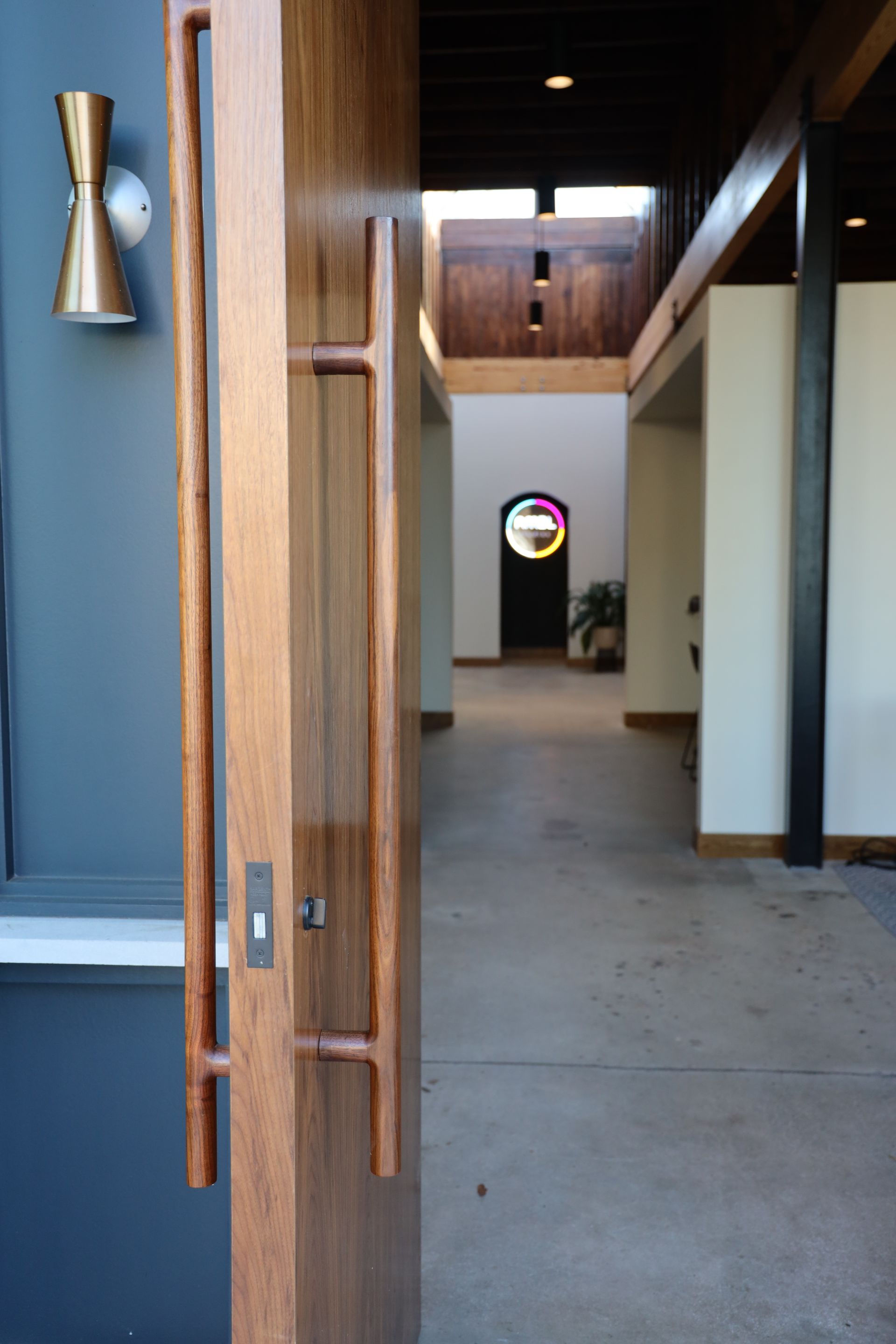 Wooden door with modern pulls, open to a hallway with a colorful stained-glass window.