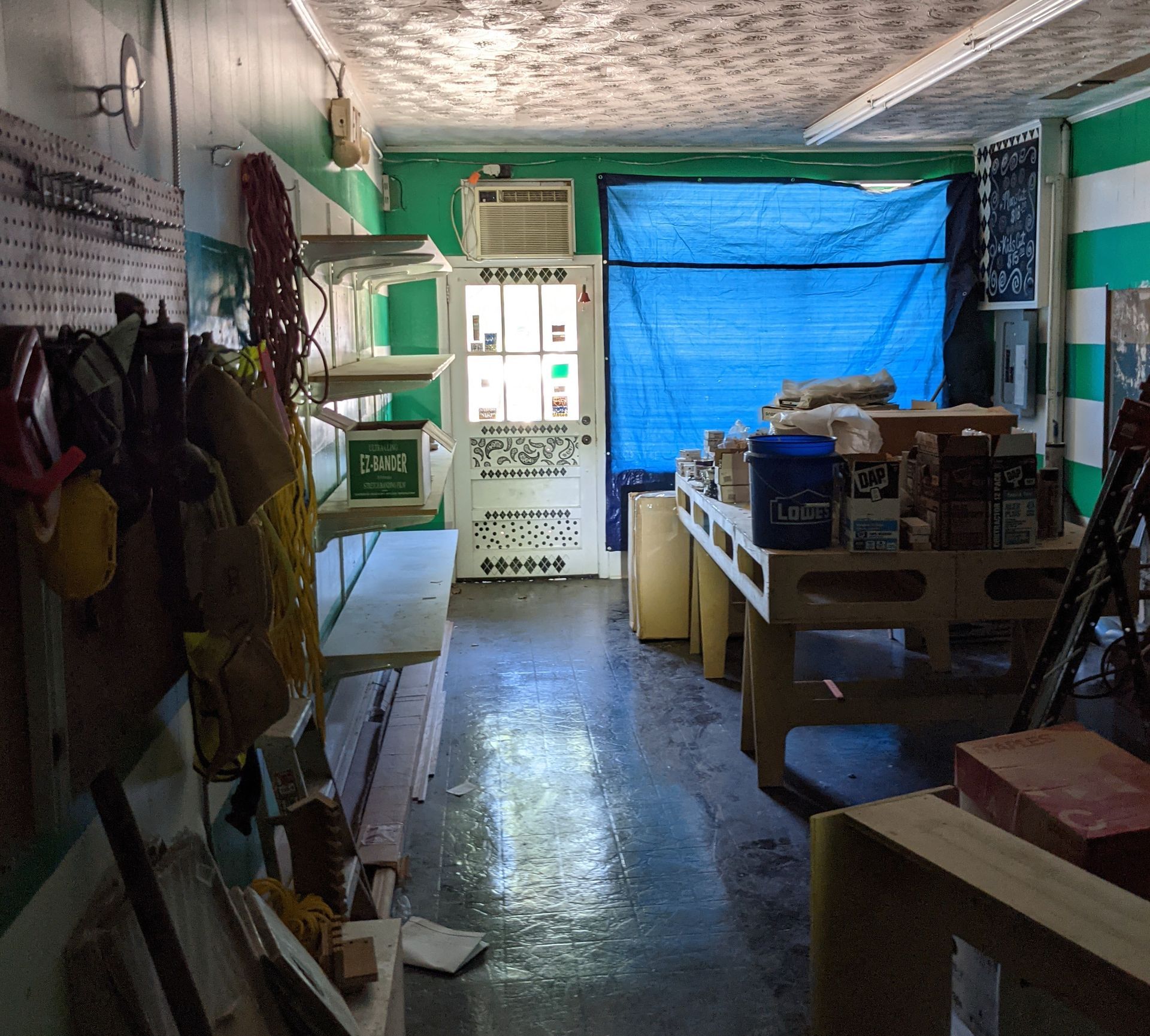 Workshop interior with tools, workbench, and blue tarp; green and white walls, cluttered and functional.