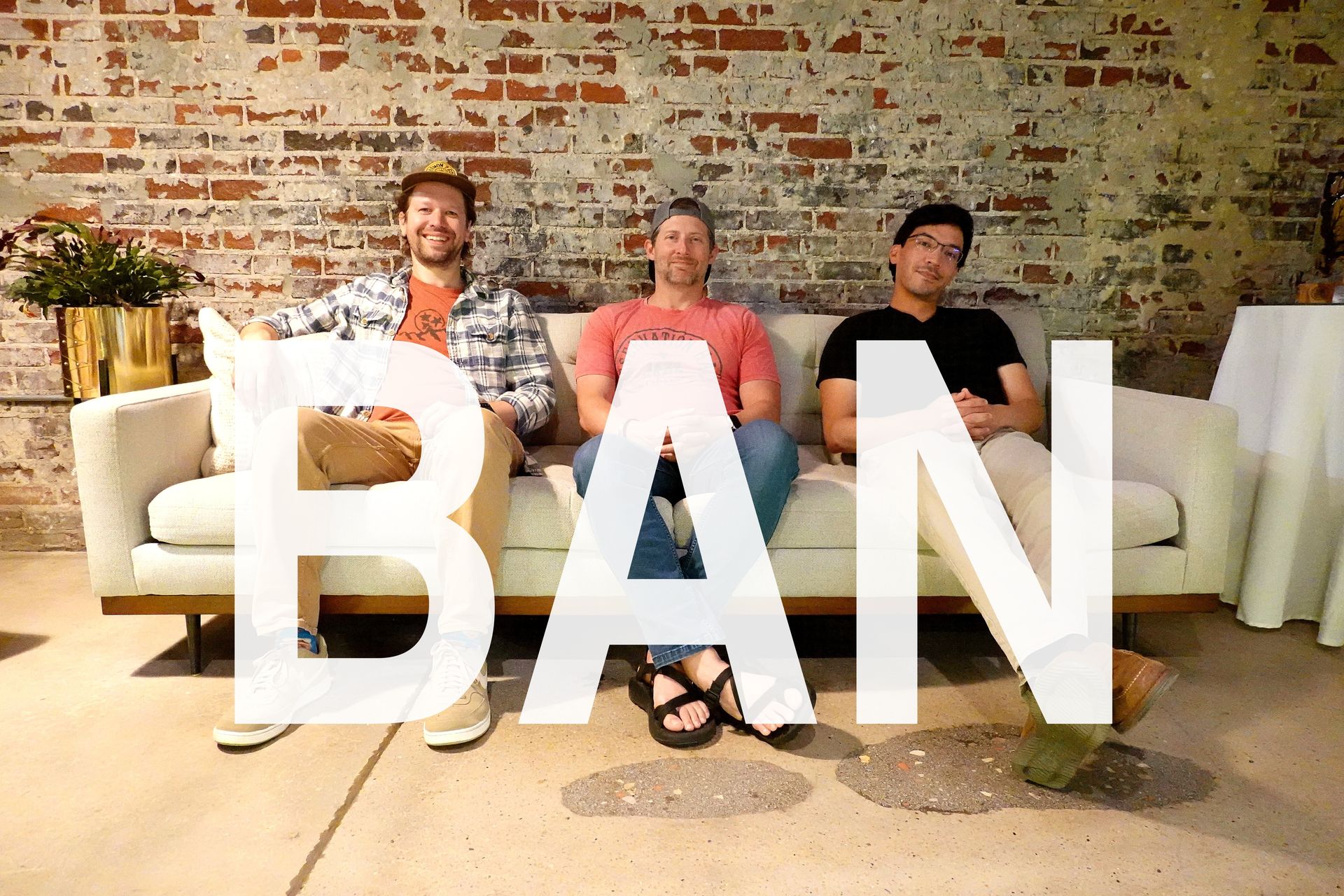 Three people sitting on a couch in a rustic room, with large white “BAN” text overlaid.