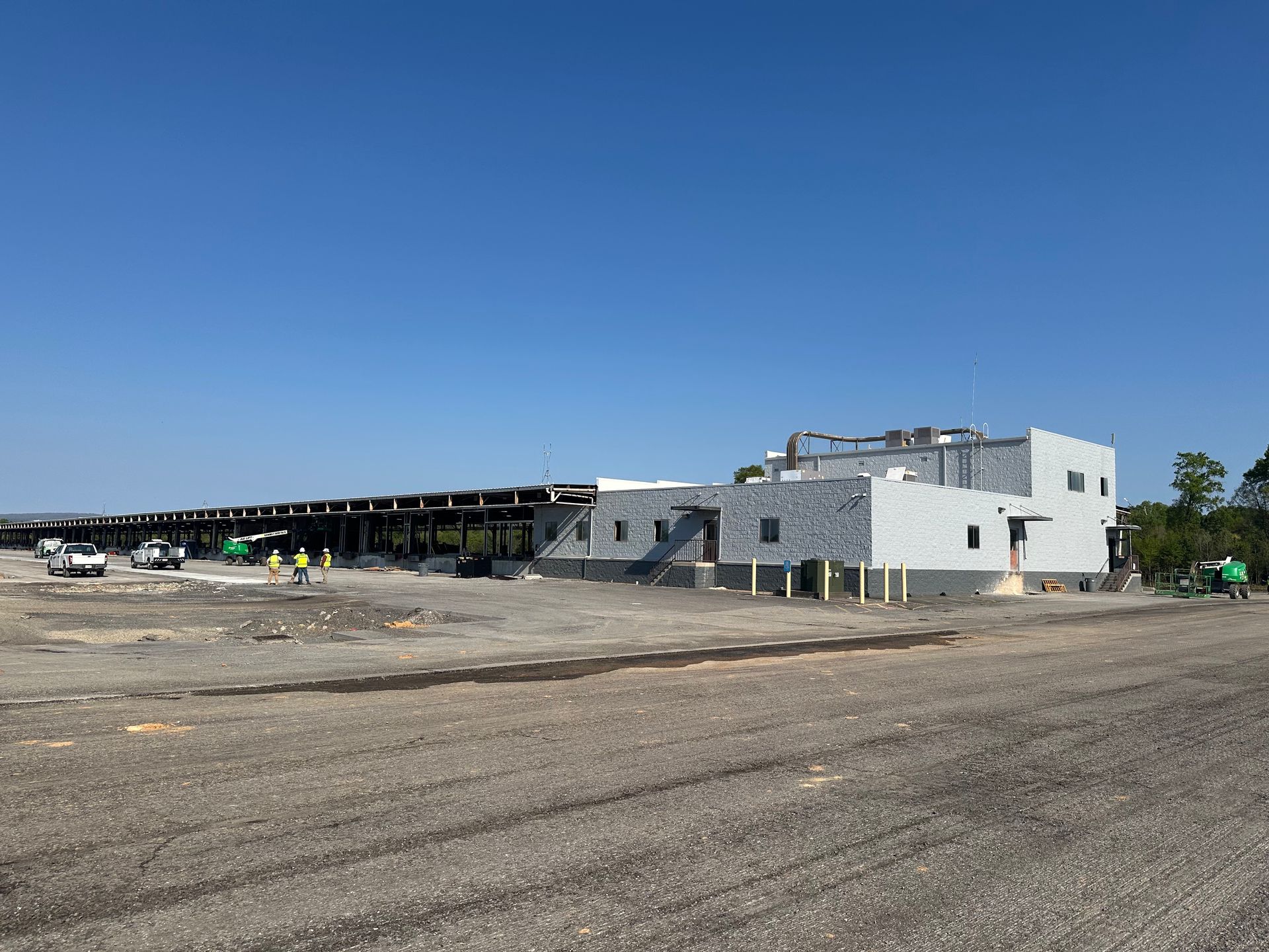 Wide dirt lot beside a low industrial building under a clear blue sky