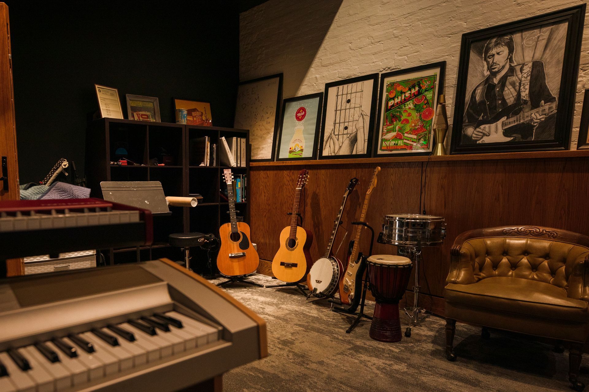 Music studio with keyboard, guitars, drums, framed art, and a leather couch on a rug.
