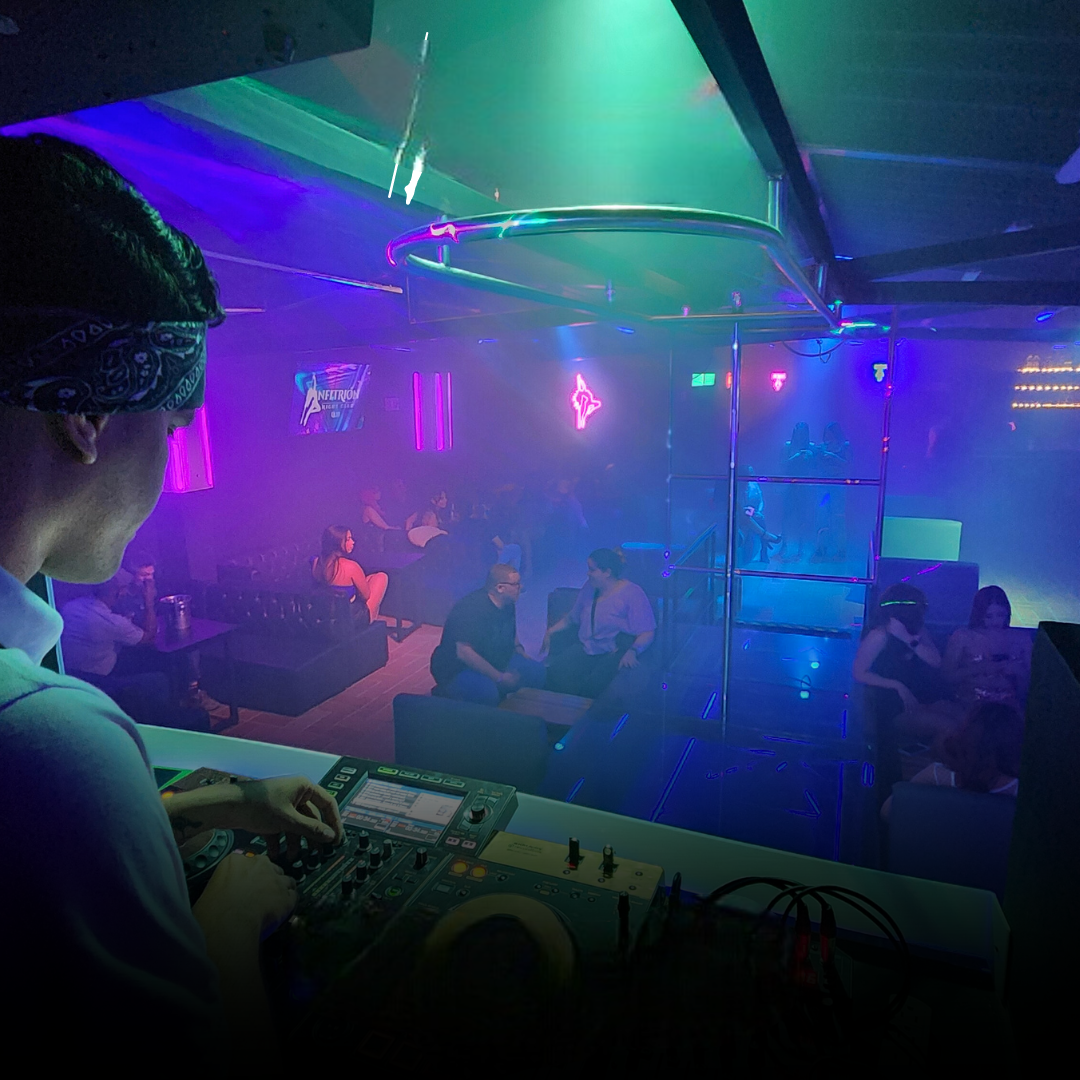 DJ en una discoteca tocando música, con una multitud de gente e iluminación colorida.