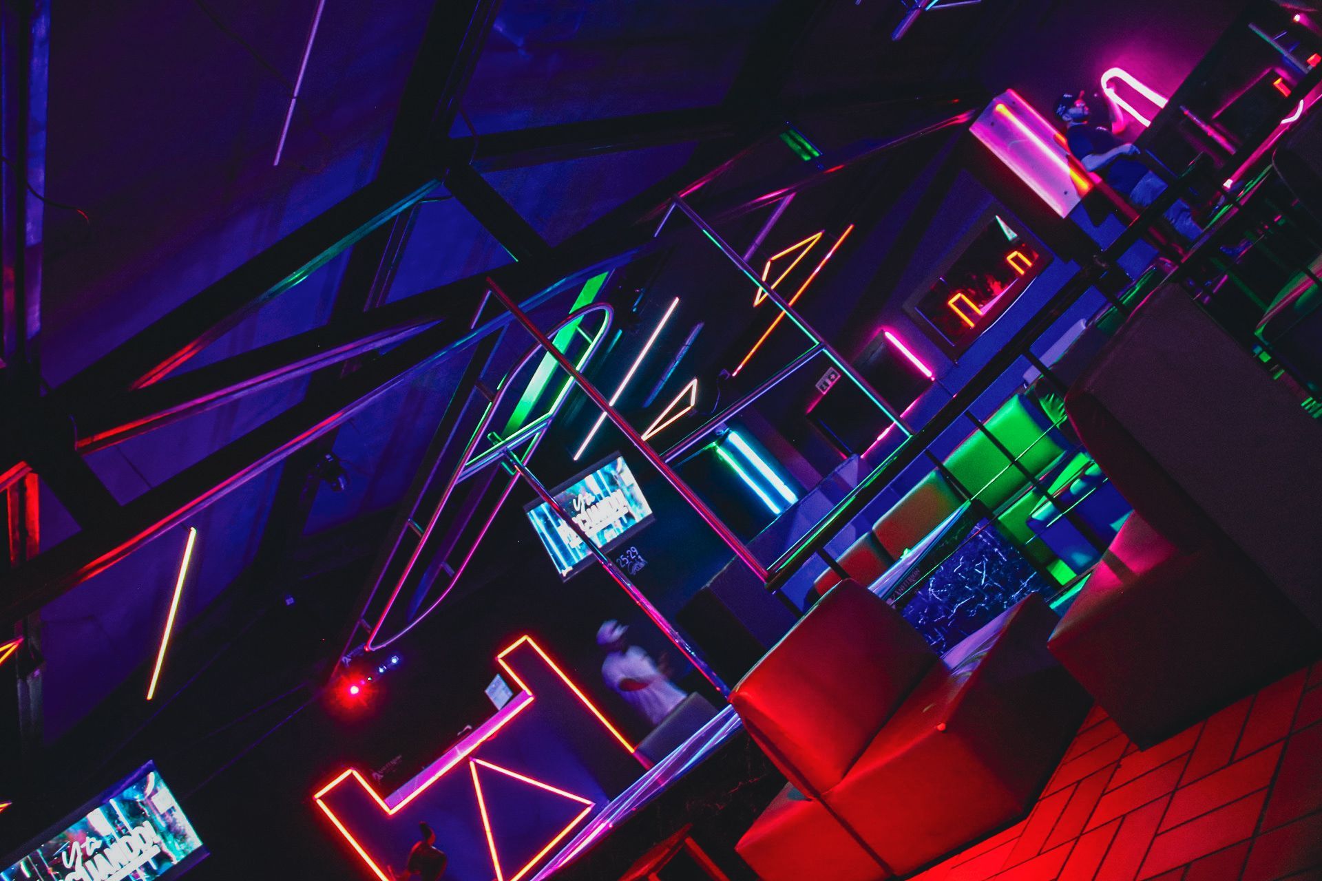 Interior del club iluminado con neón, asientos rojos y luminarias geométricas.