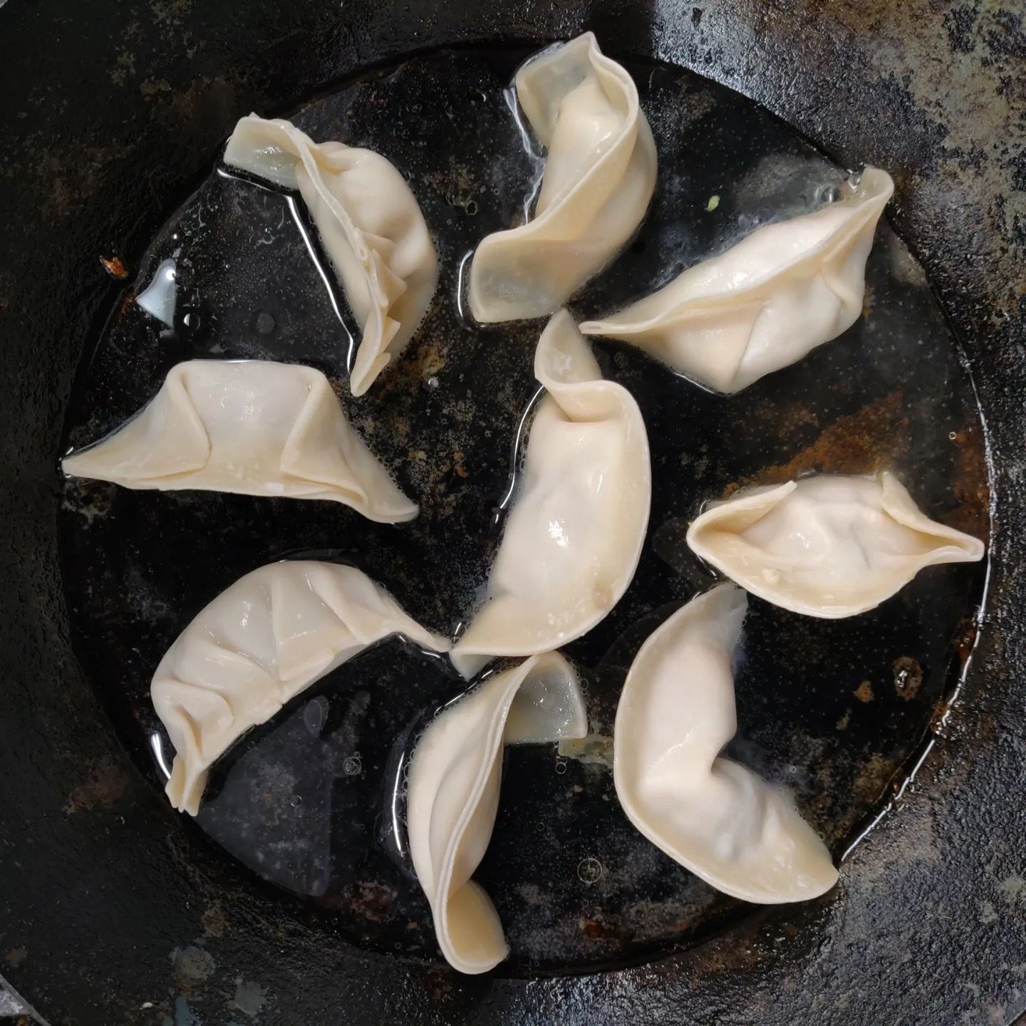 A bunch of dumplings are cooking in a pan