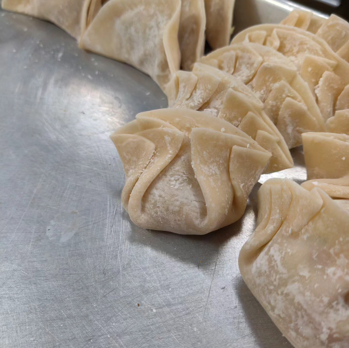 A bunch of dumplings are sitting on top of a metal tray.