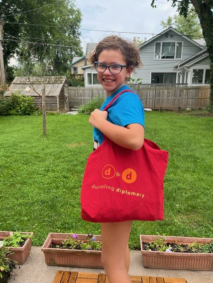 A young girl wearing glasses is holding a red tote bag.