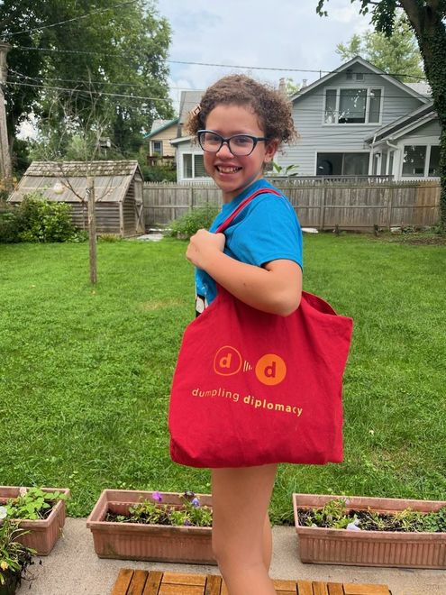 A young girl wearing glasses is holding a red tote bag.