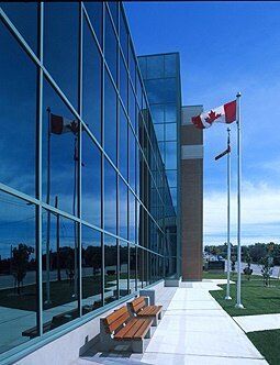 Modern glass building with Canadian flags waving in the wind, sunny day.
