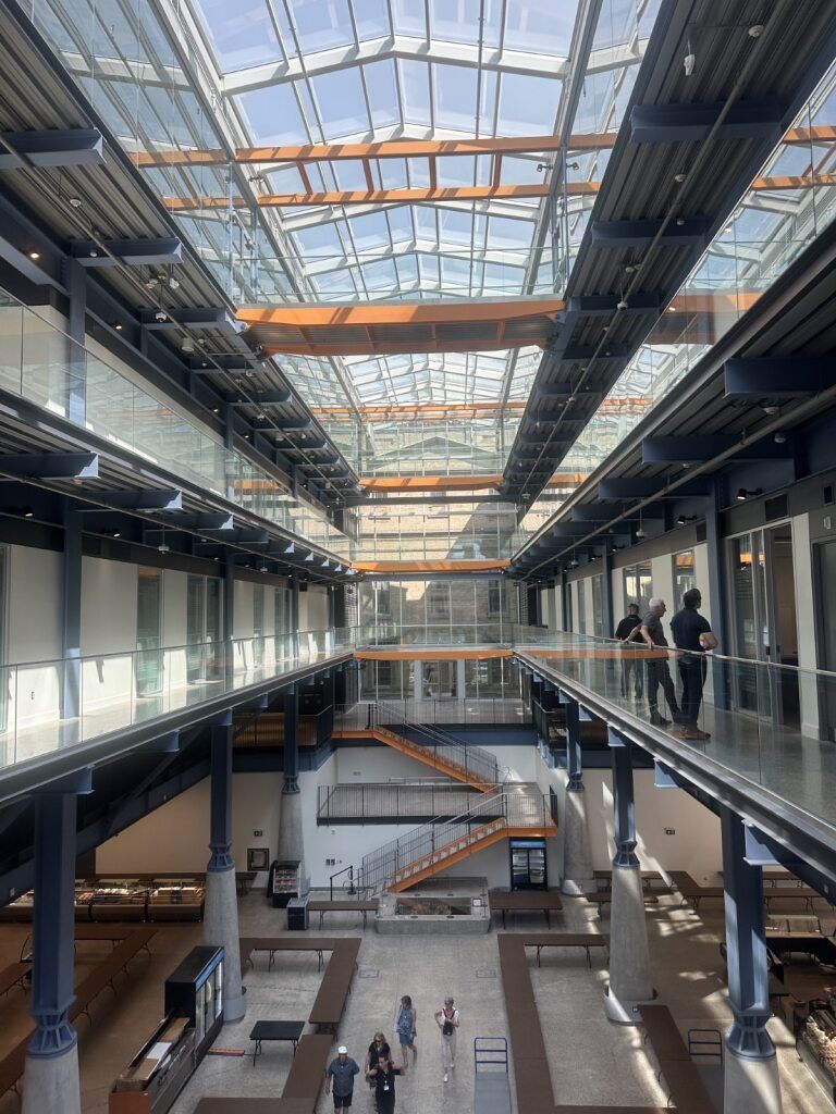 Interior of a modern building with glass ceiling, multiple levels, and people walking.
