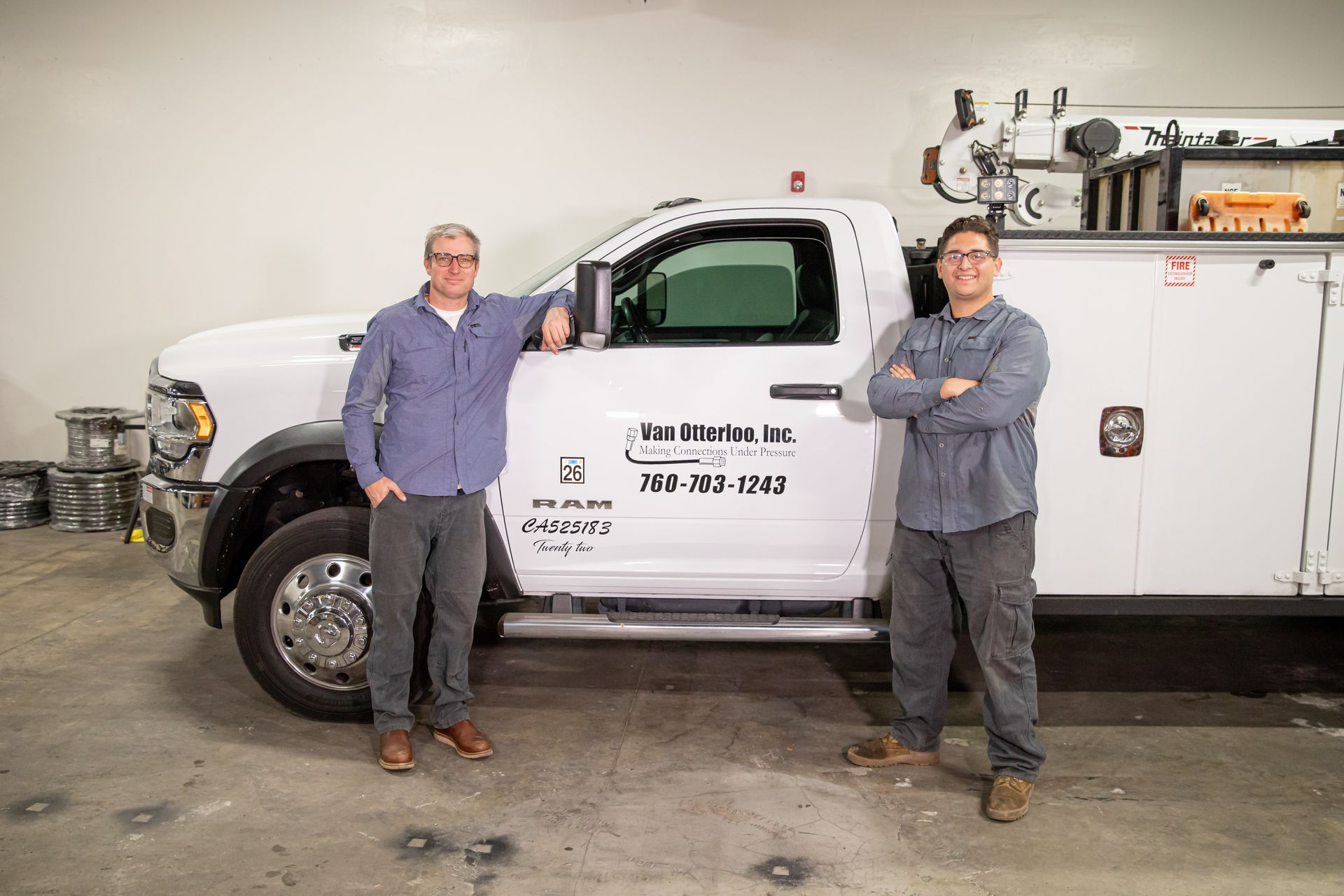 Two men are standing next to a white truck with the Van Otterloo, Inc. logo on it in a workshop.